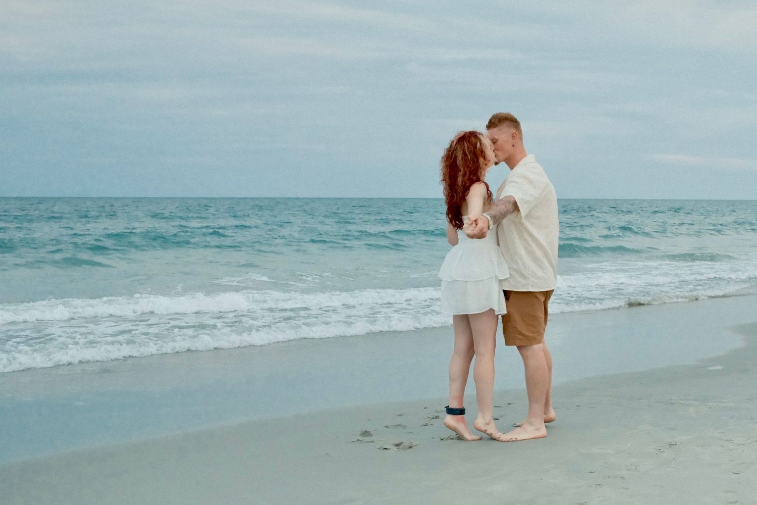 A romantic couple walks along the shoreline during a beach sunset photo session.