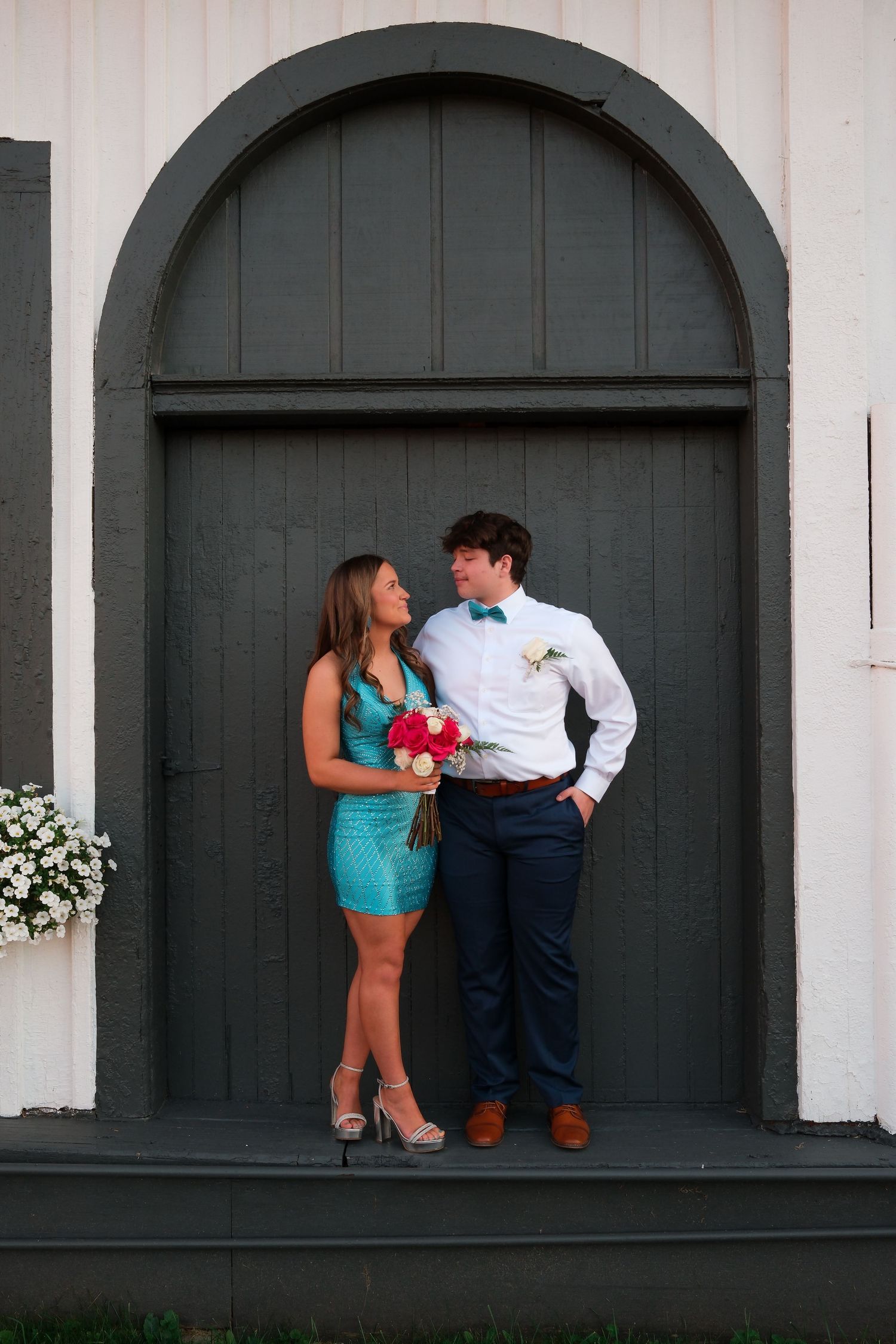 A couple poses in front of dark archways wearing formal attire with turquoise and navy blue accents.