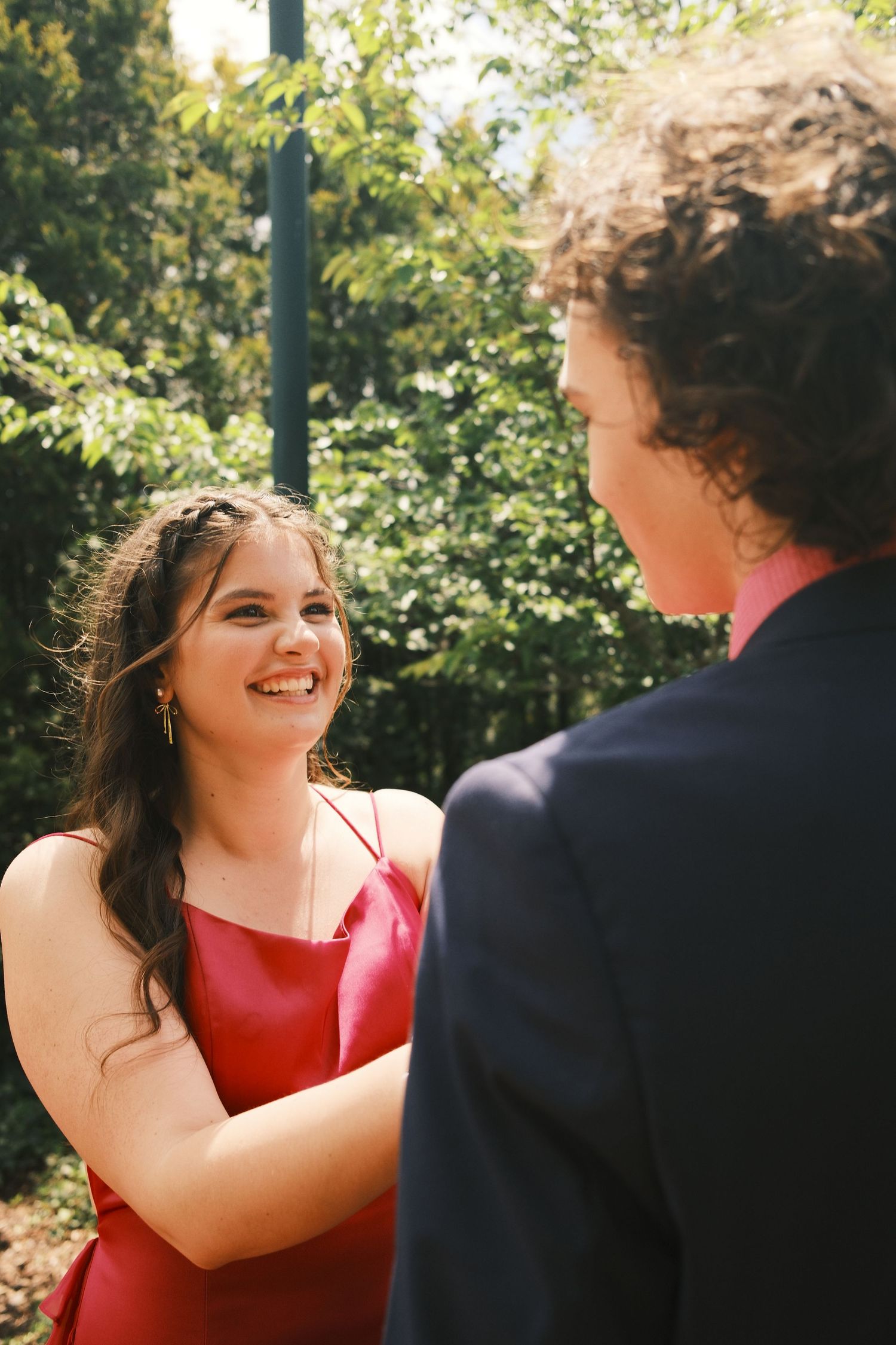 A couple shares a joyful moment outdoors with lush greenery in the background.