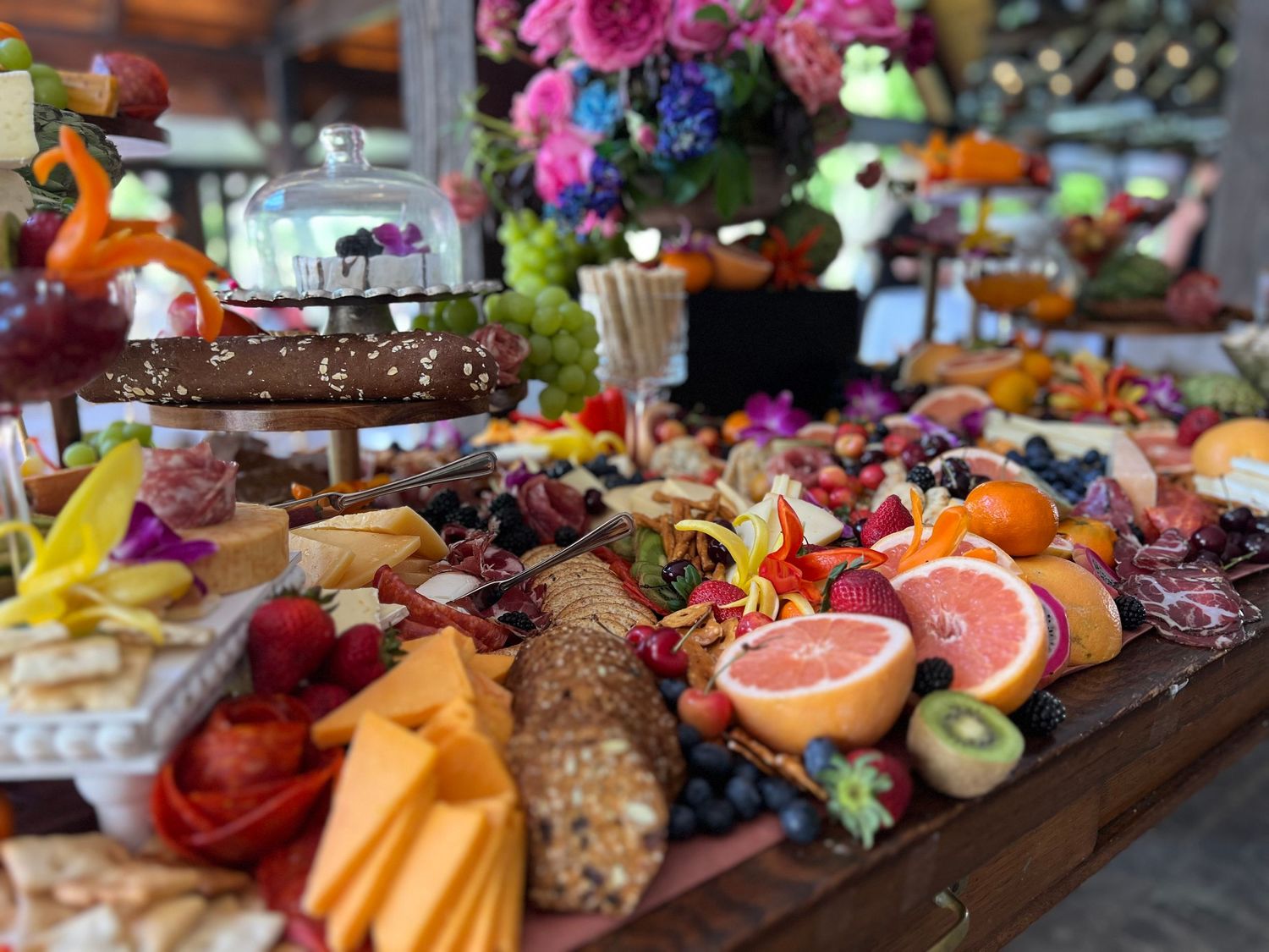 Colorful charcuterie board displays an array of fruits, meats, cheeses and garnishes on a wooden surface.