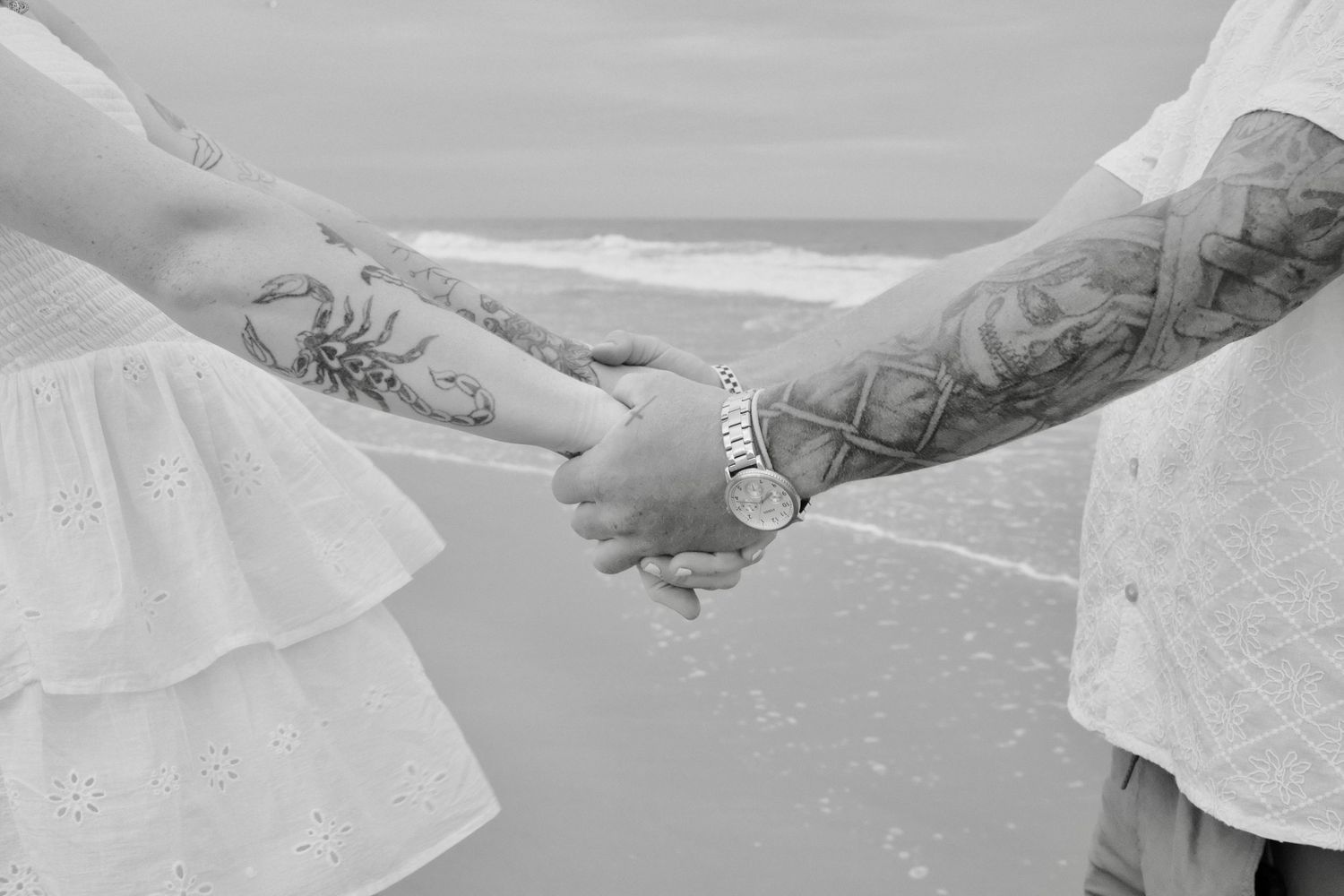 Two tattooed hands holding a white veil against a cloudy sky background.