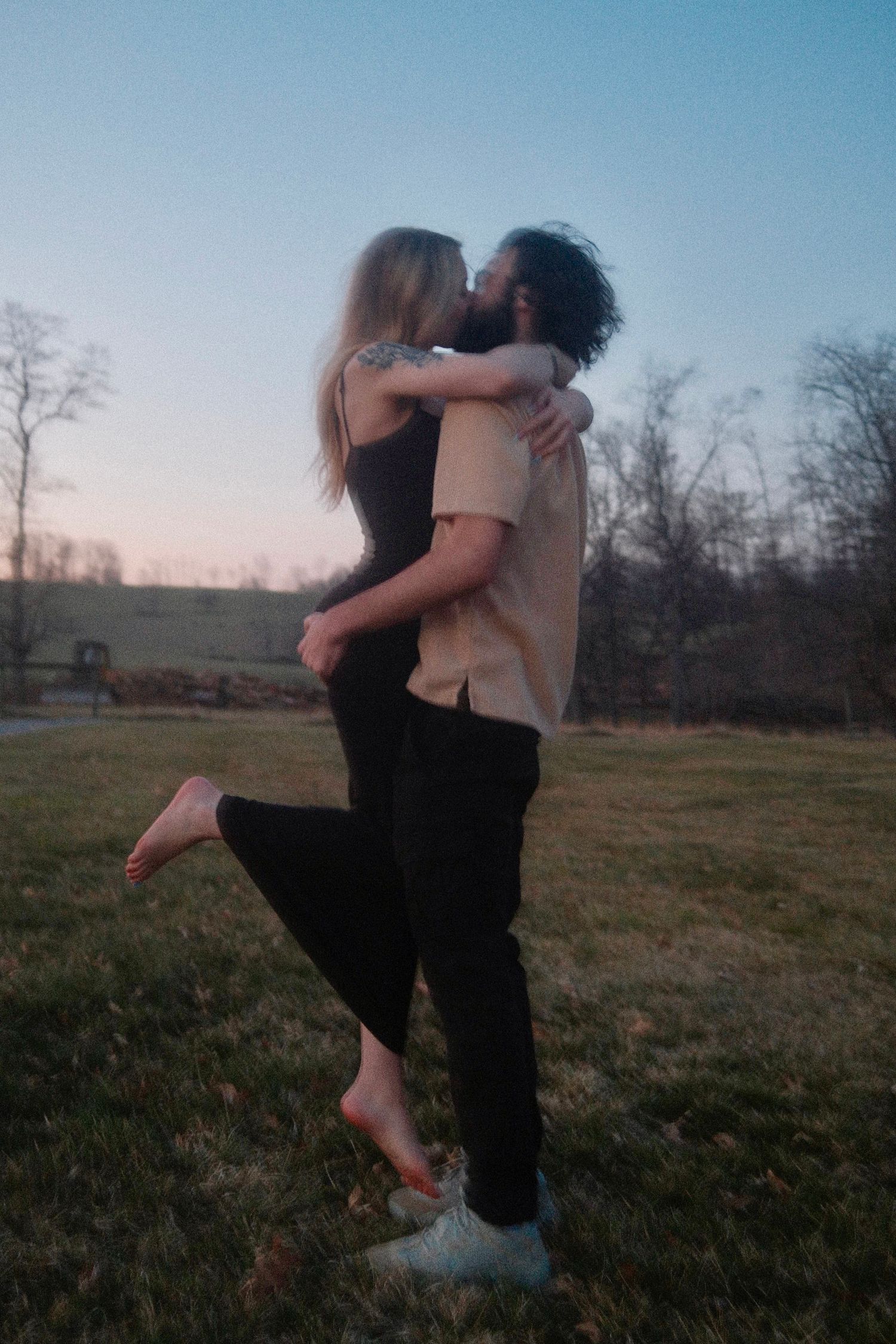 Two people embrace and dance together in a grassy field at sunset creating a romantic silhouette against the sky.