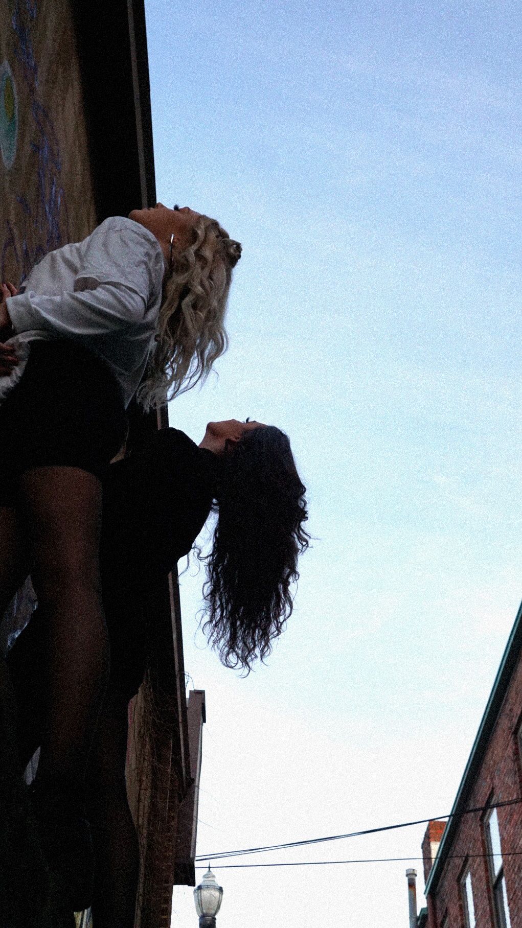 Two silhouettes against a blue sky between brick buildings with a street lamp visible in the distance.