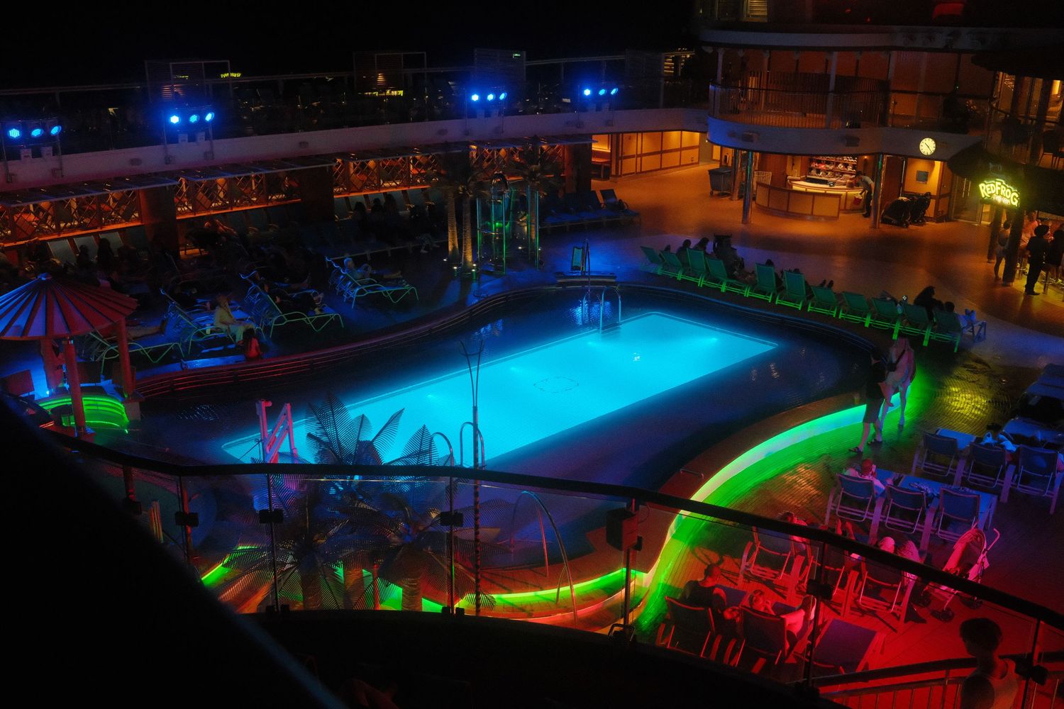 Colorful nighttime pool area illuminated with vibrant blue, red, and green lighting creating a festive atmosphere.
