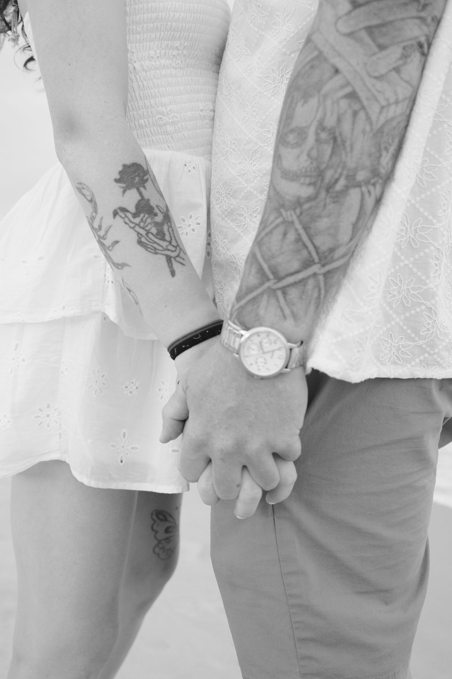 Close-up view of tattooed arms and hands holding each other against a white background.