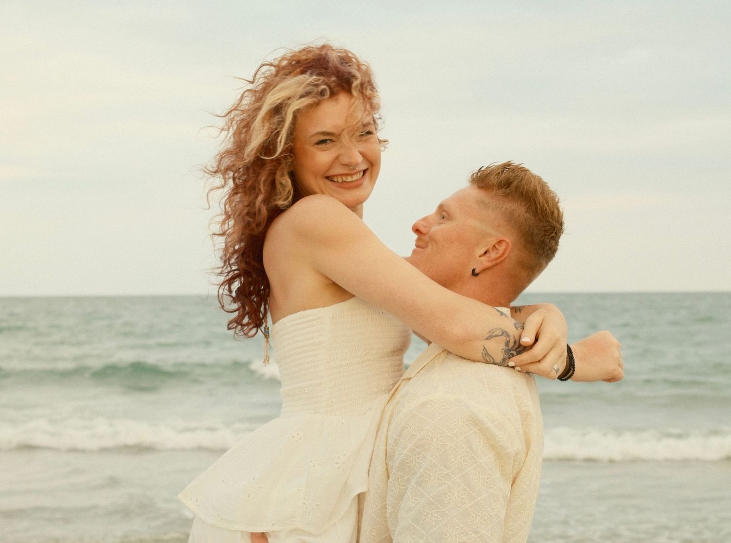 A couple embraces and laughs together during their beach photoshoot.