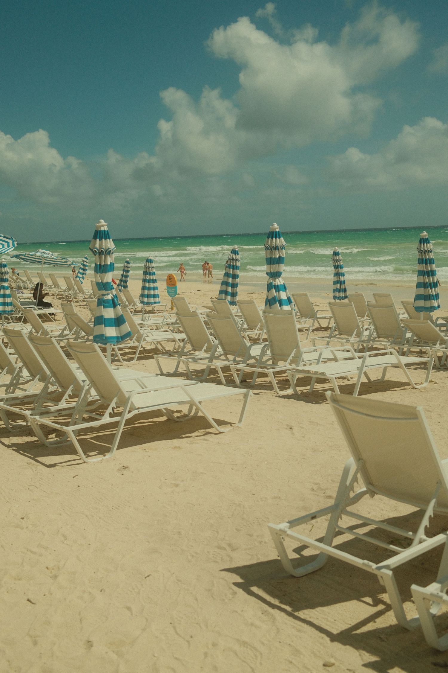 Empty beach chairs with blue striped umbrellas lined up on white sandy shoreline.