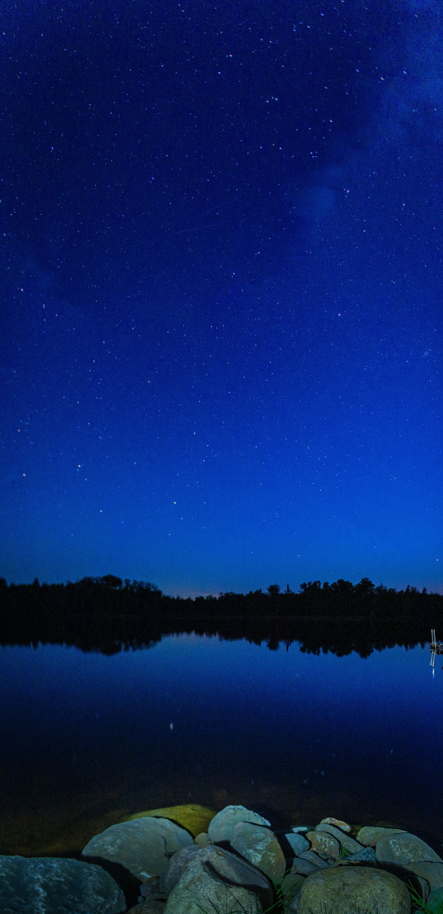 A starry sky over a lake with rocks as the foreground in Northern Minnesota.