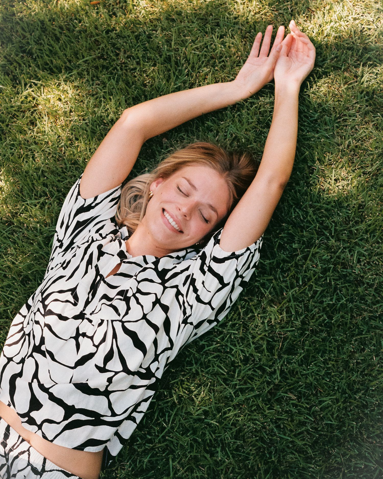 Natural light photo of girl lying in green grass, joyful expression, photographed by Sadie Sanders Photography