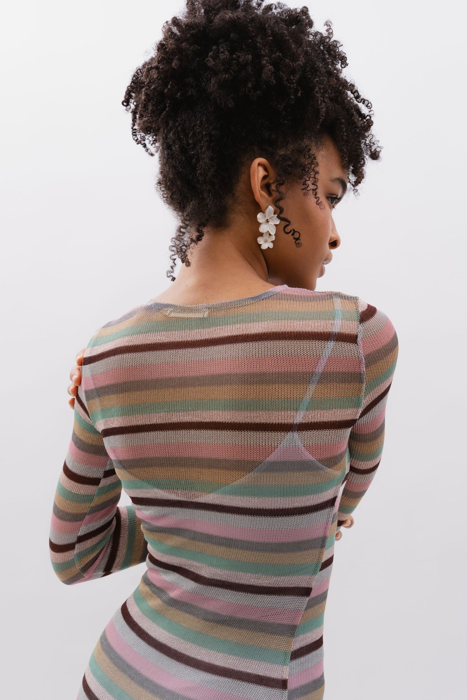 Female model posing against white background in striped dress, earring details emphasized, photographed by Sadie Sanders