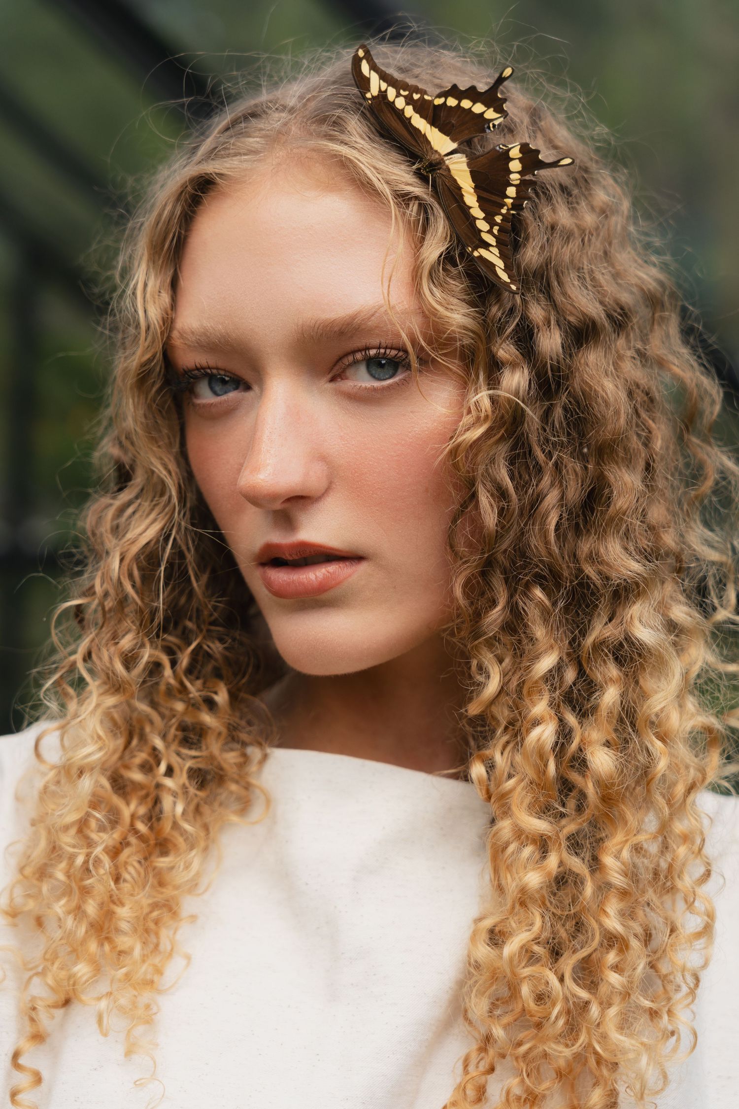 Female model with butterfly in hair posing in greenhouse, styled fashion shoot by Sadie Sanders Photography