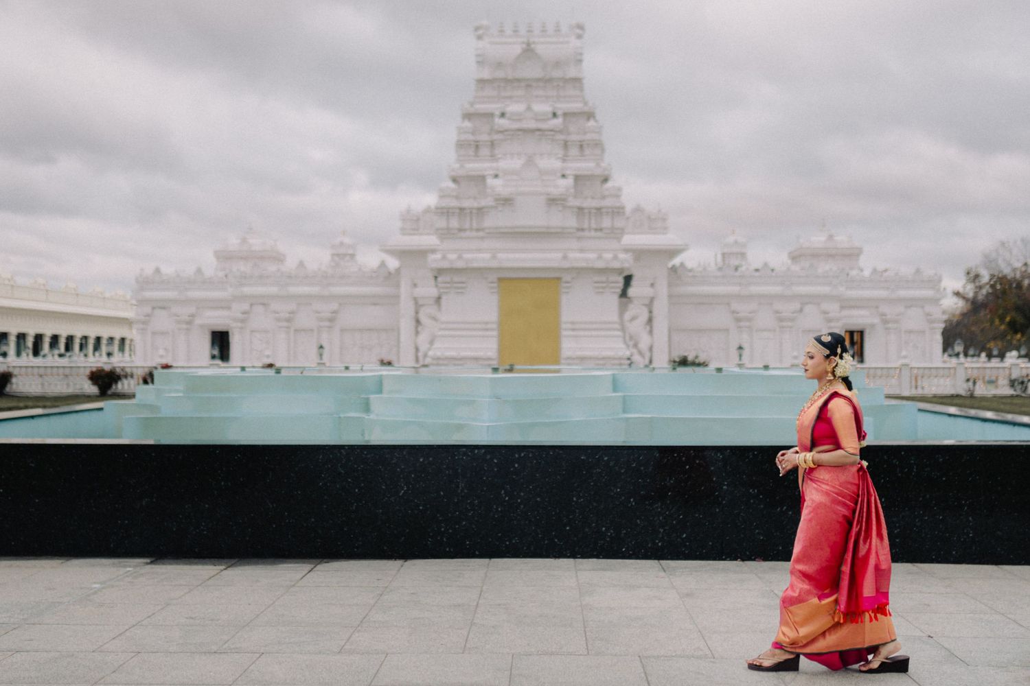 Modern temple architecture with white stone structures against cloudy sky.