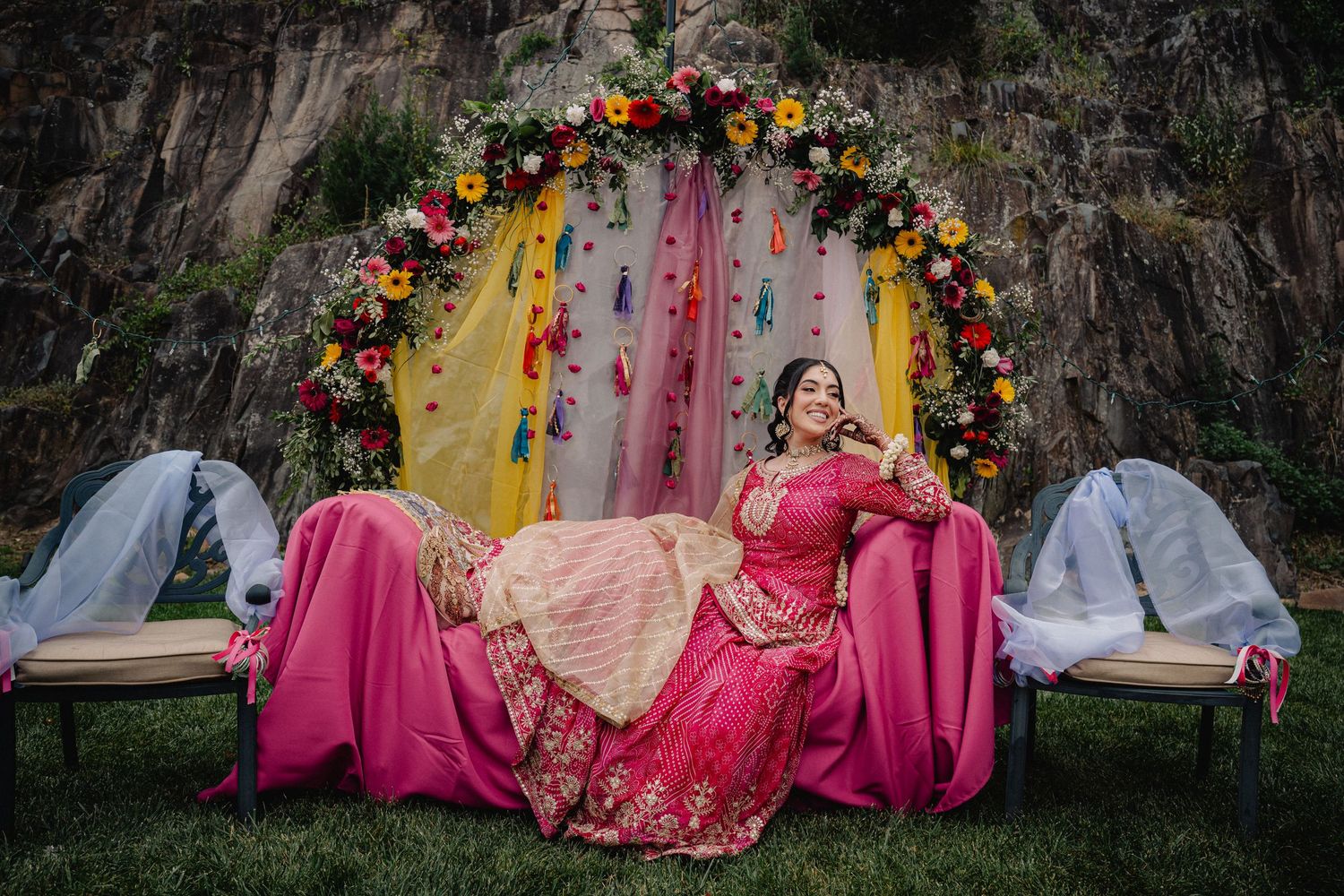 Wedding decor with vibrant floral arrangements and pink fabric draping against trees.