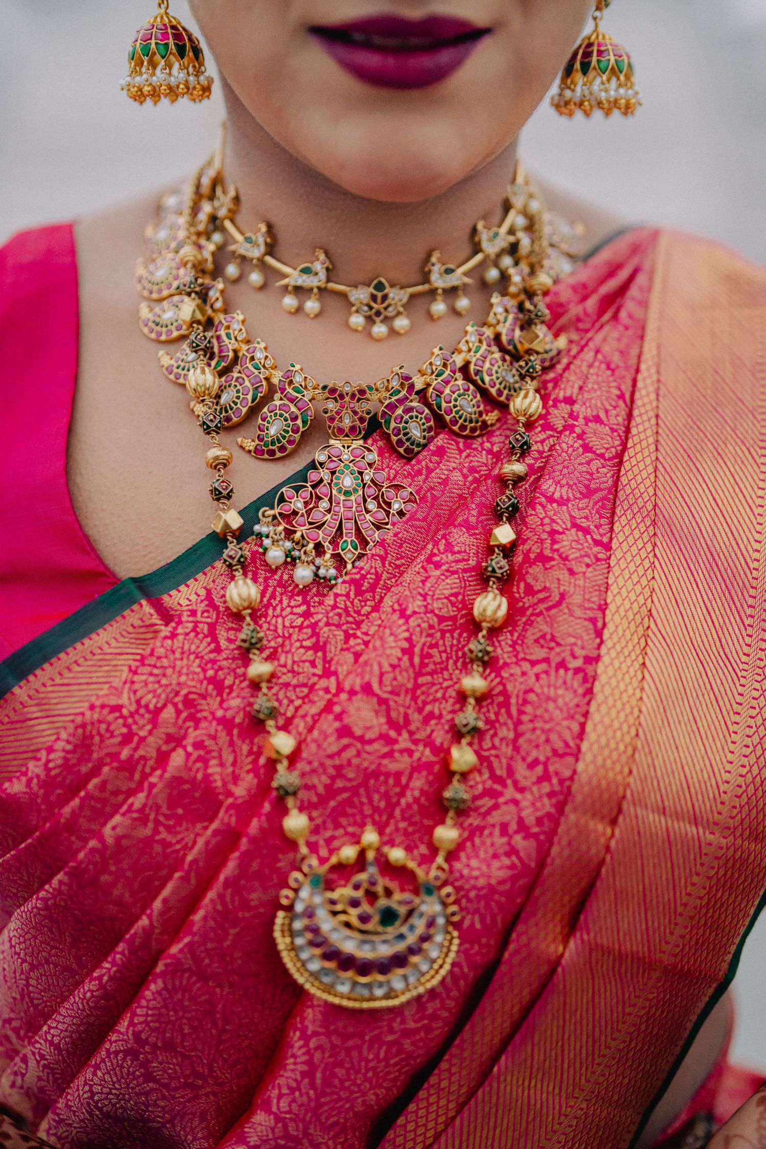 Close-up of ornate gold and pearl traditional Indian bridal jewelry with pink silk saree.