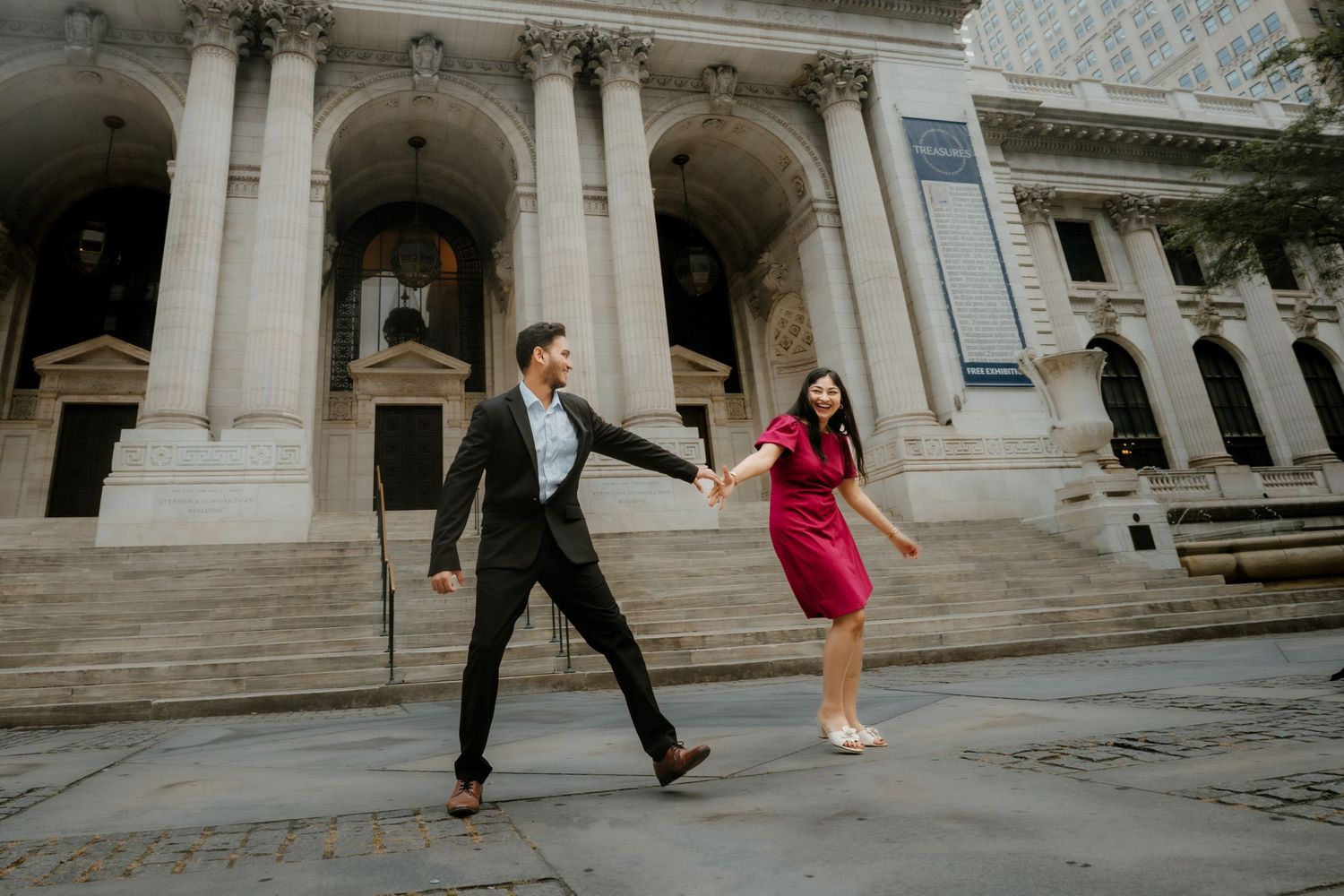 Two people walk past grand stone columns and architecture at the New York Public Library entrance.