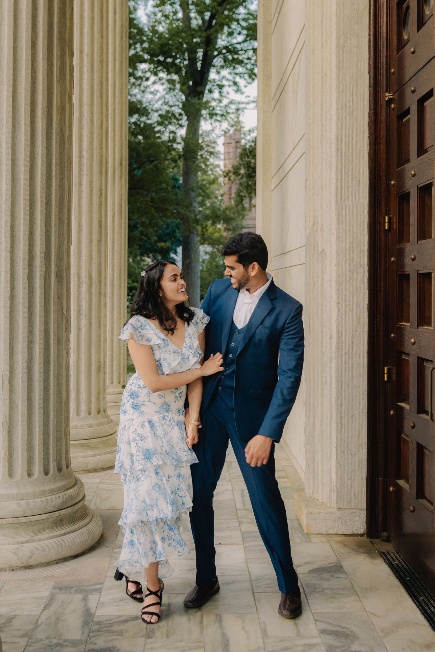 A couple shares a romantic moment between classical columns during an engagement photo session at a historic building.