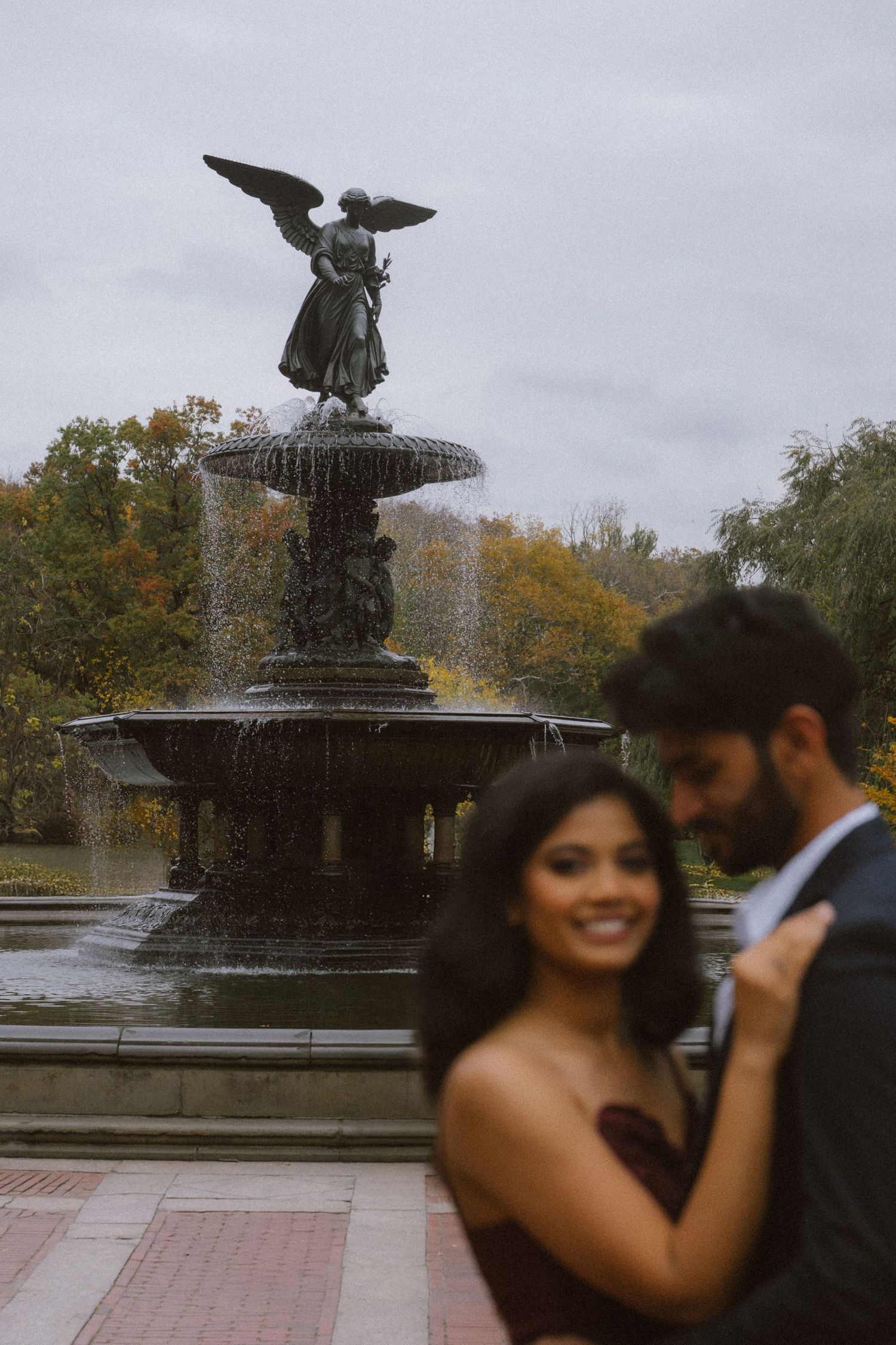 Romantic couple photoshoot by an ornate fountain in a park during autumn.