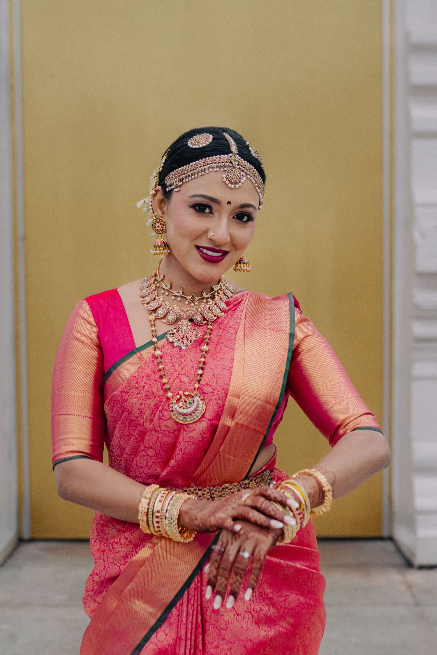 Traditional South Indian bride in pink silk saree with gold jewelry and temple headpiece.