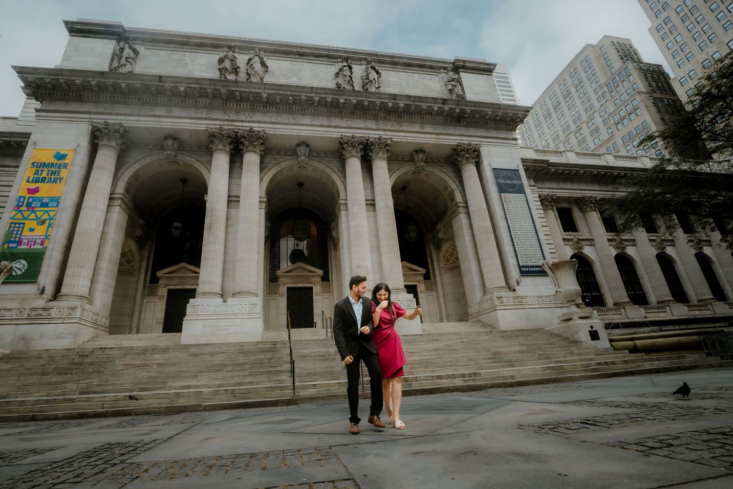 A couple poses on the steps of the New York Public Library's grand marble entrance with its iconic columns.