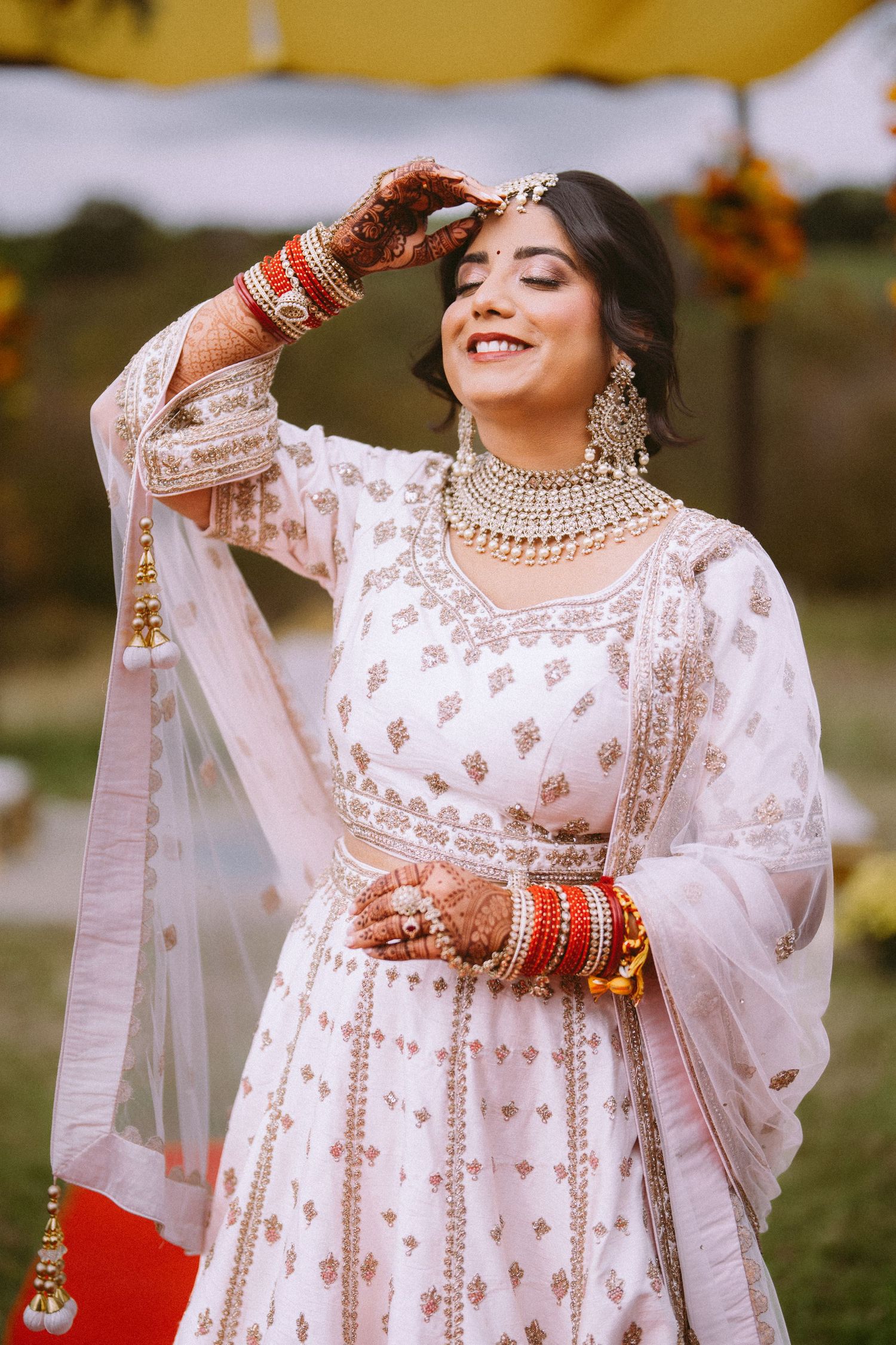 Traditional Indian bridal attire featuring a white embroidered lehenga with red bangles and jewelry.