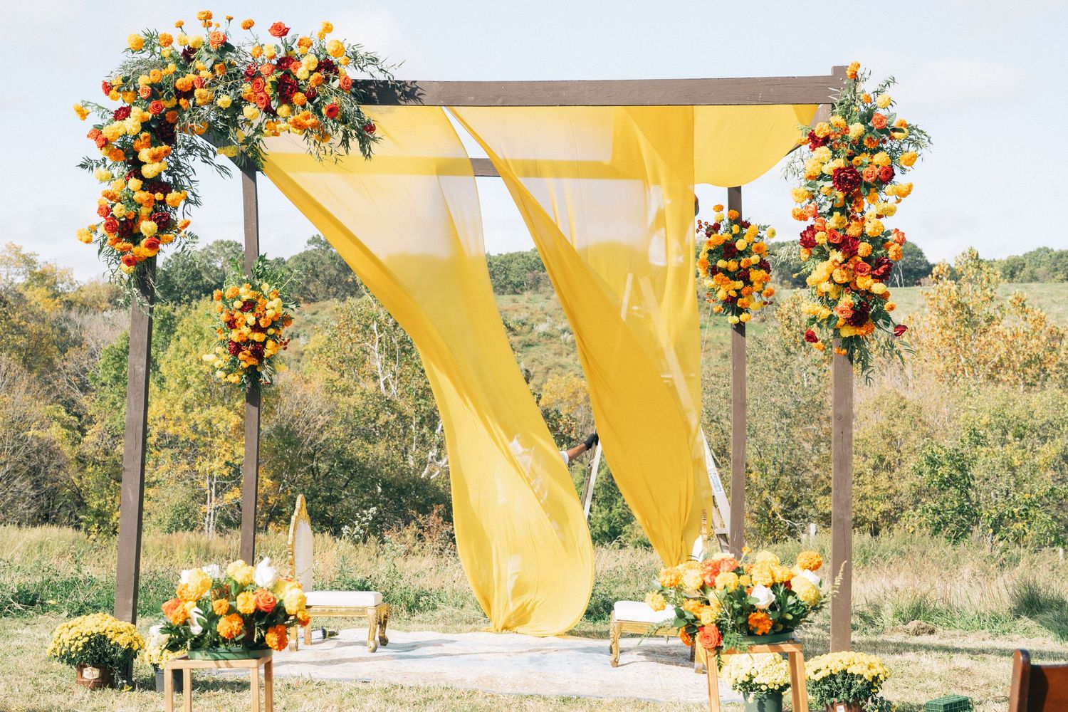 Outdoor wedding setup with yellow drapes and autumn floral arrangements.