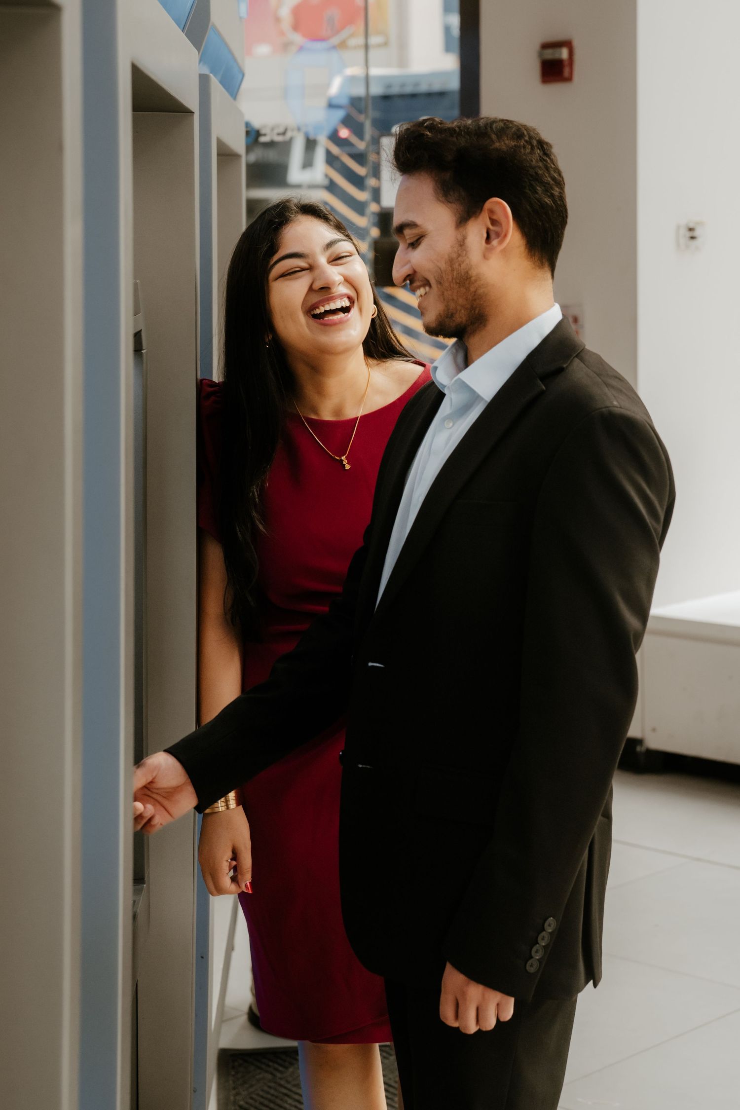A couple in formal attire shares a joyful moment together in a bright hallway.