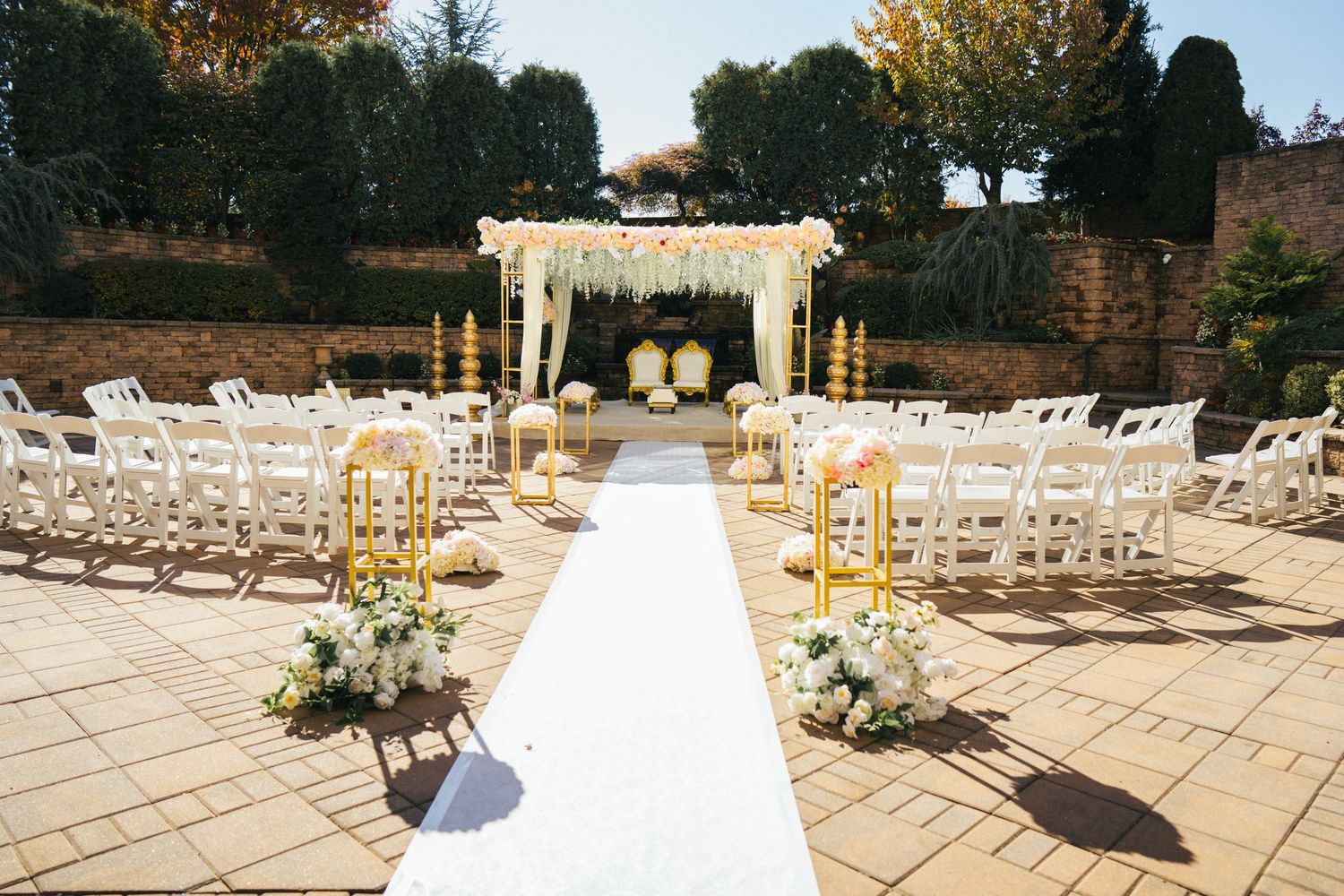 White chairs arranged outdoors for an elegant wedding ceremony with golden decor elements.