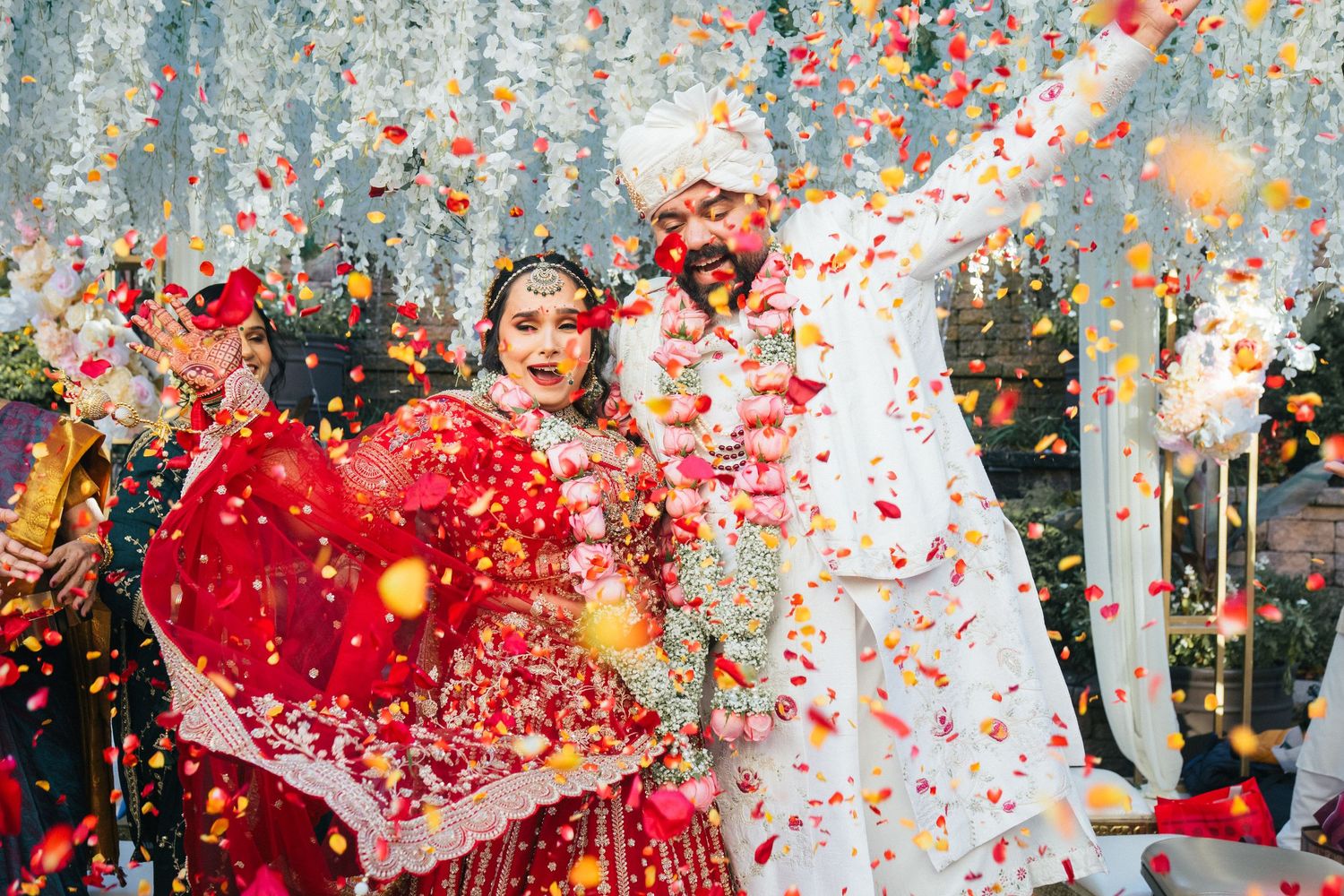 Celebratory moment with red confetti and flower petals raining down during wedding festivities.
