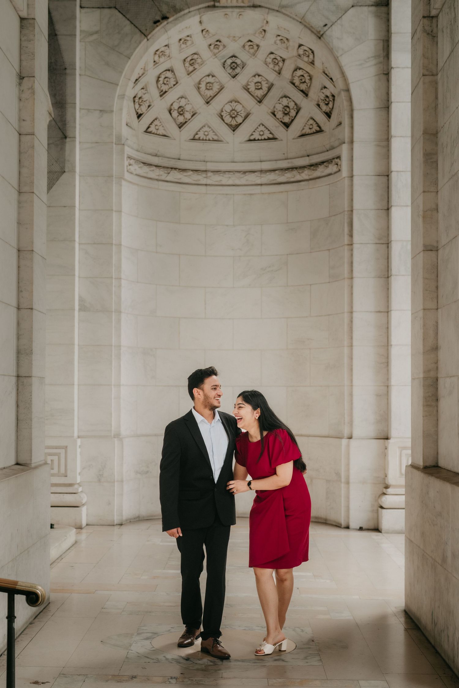 A couple in formal attire shares romantic moments in an elegant white archway corridor with ornate ceiling details.