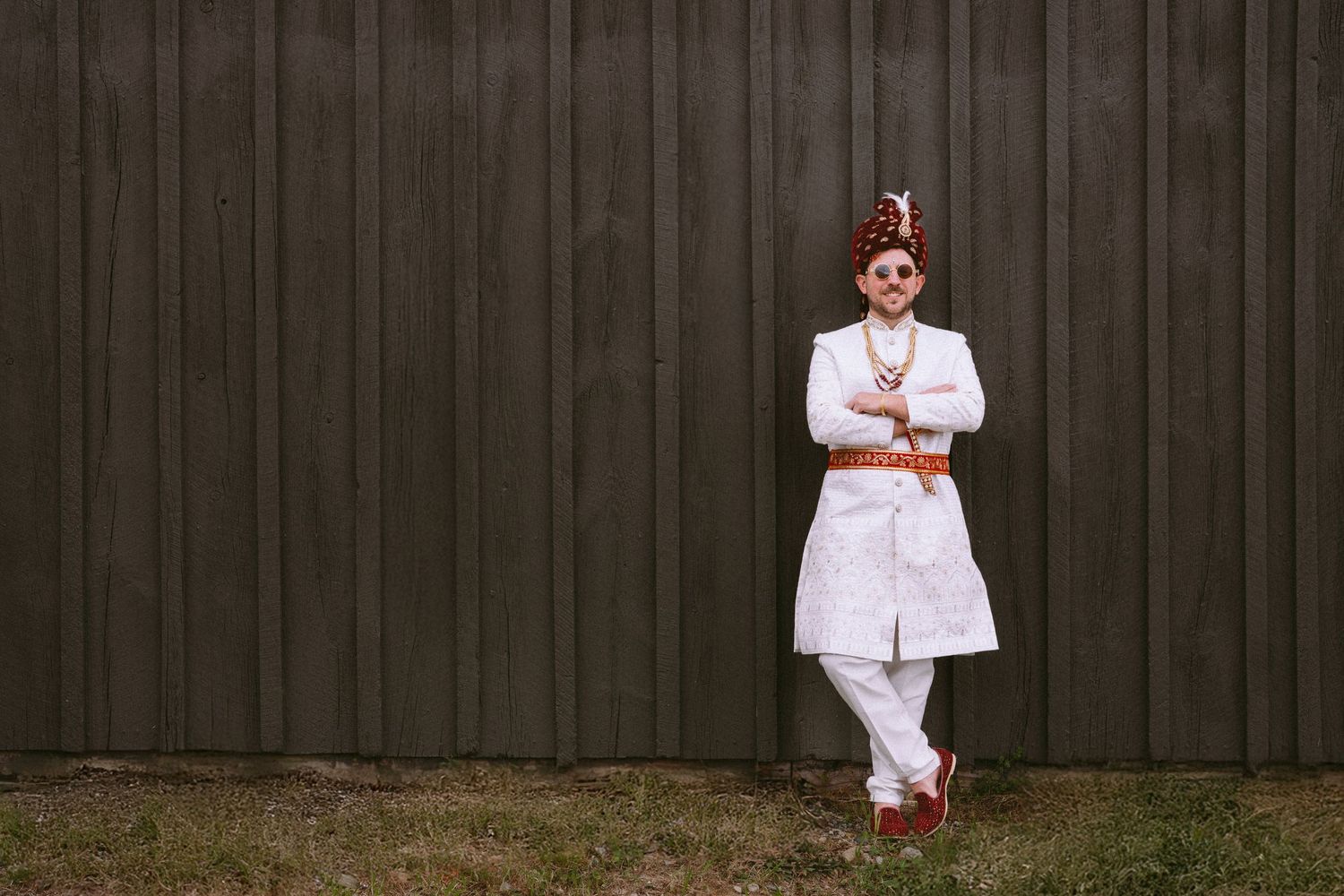 A person in a white outfit poses against a dark wooden fence in five different playful positions.