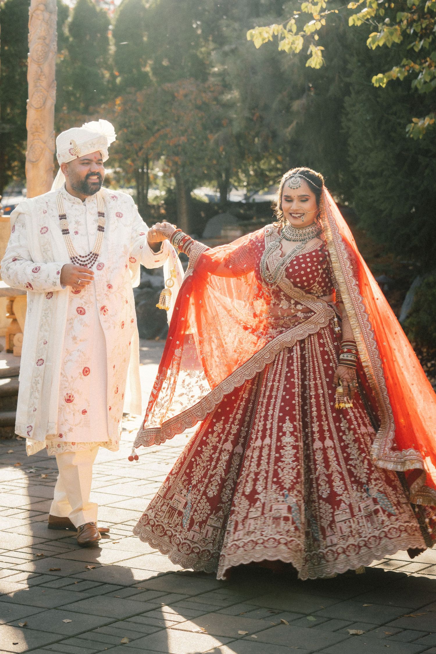 Traditional Indian wedding couple dancing in a sunlit outdoor venue.