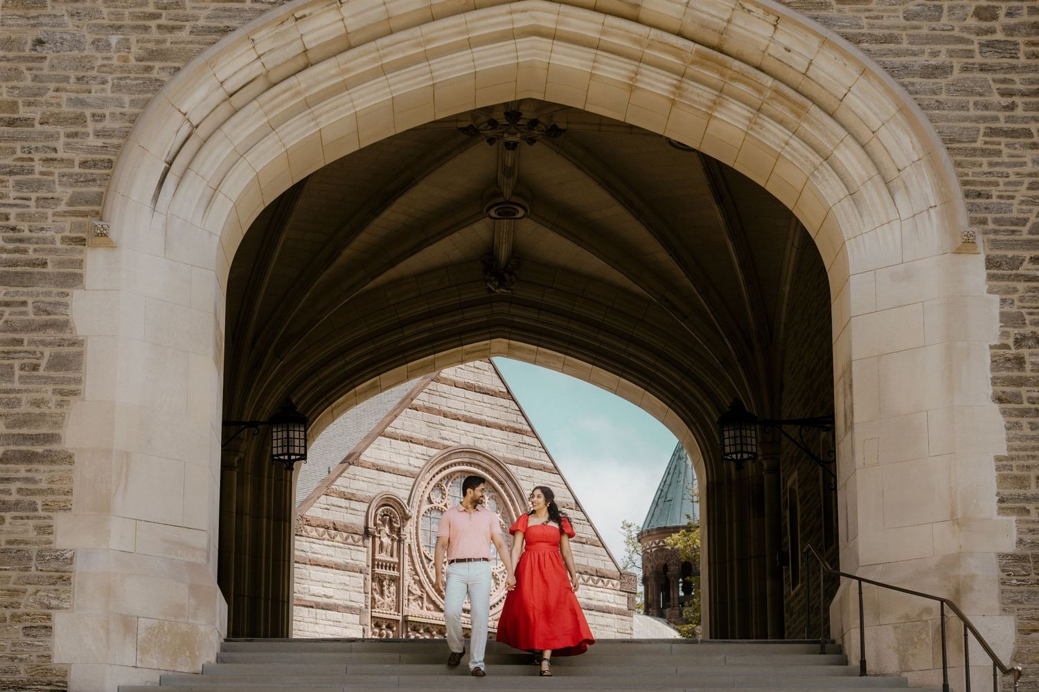 Architectural view of a stone archway corridor with brick walls and a person walking in red attire.