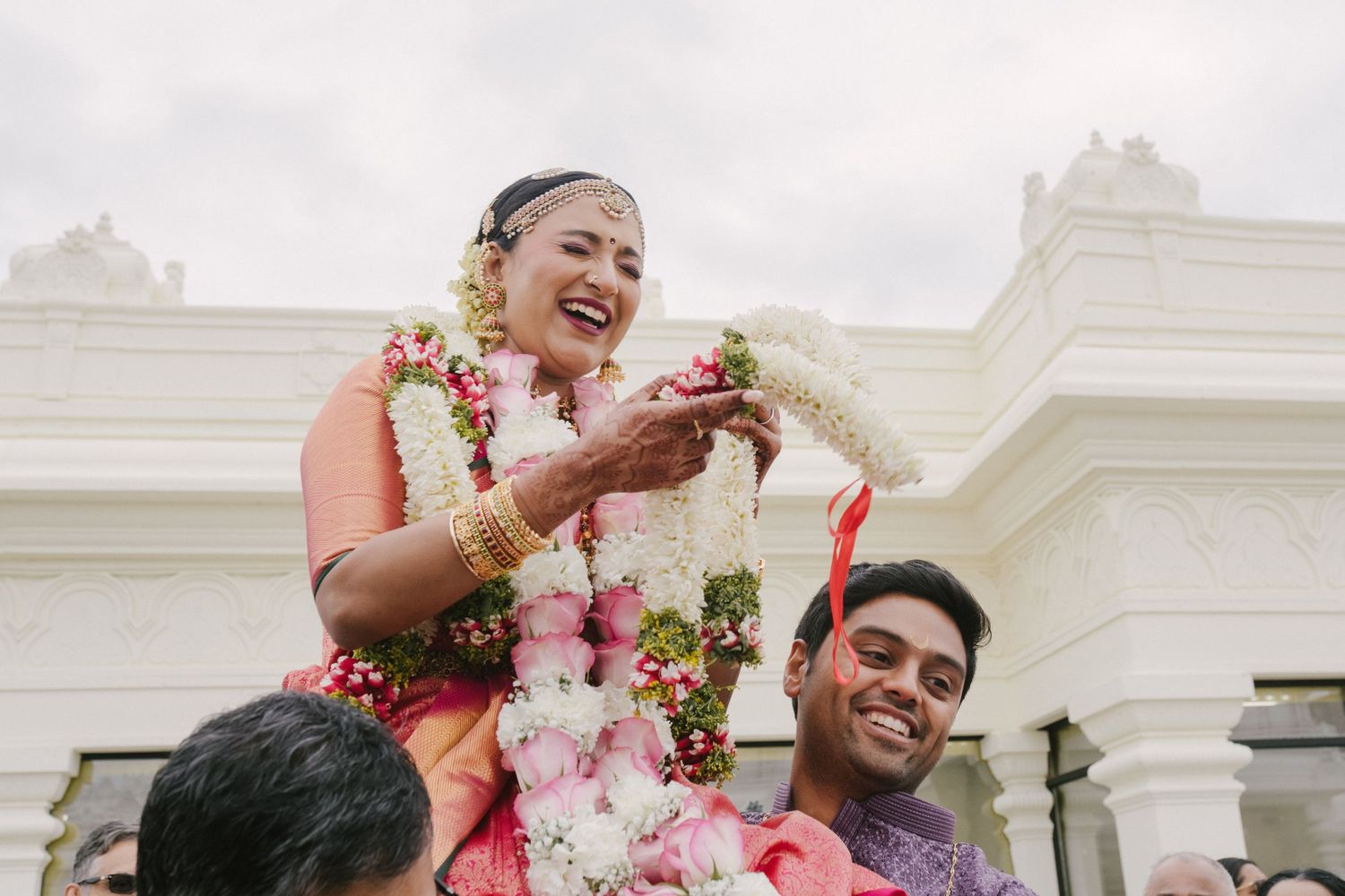 Joyful wedding celebration with flower garlands and traditional ceremonies at an elegant white venue.