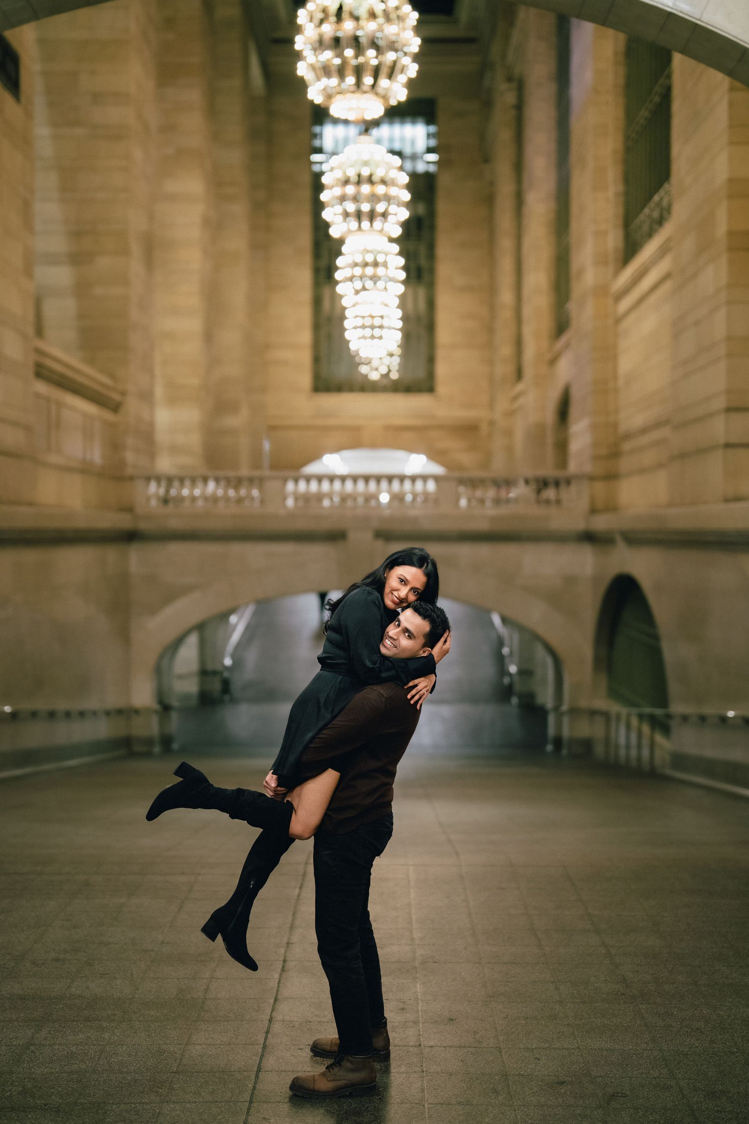 Two people dancing together in a grand hall with ornate chandeliers and stone architecture.
