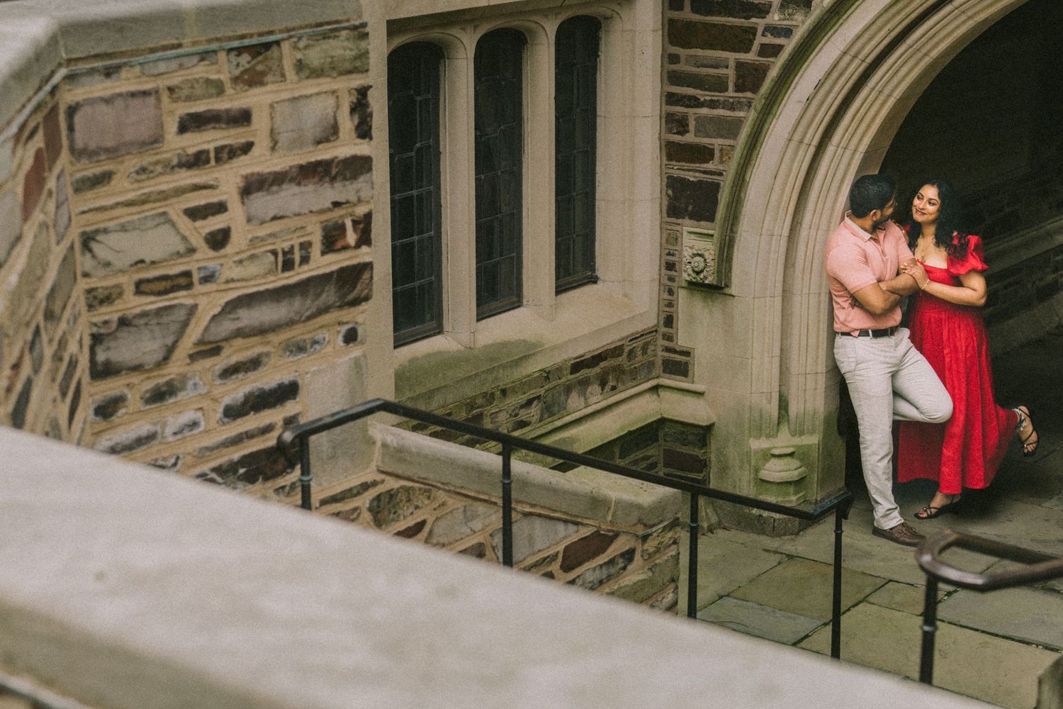 A couple in formal attire poses on the stone steps of a historic church building.