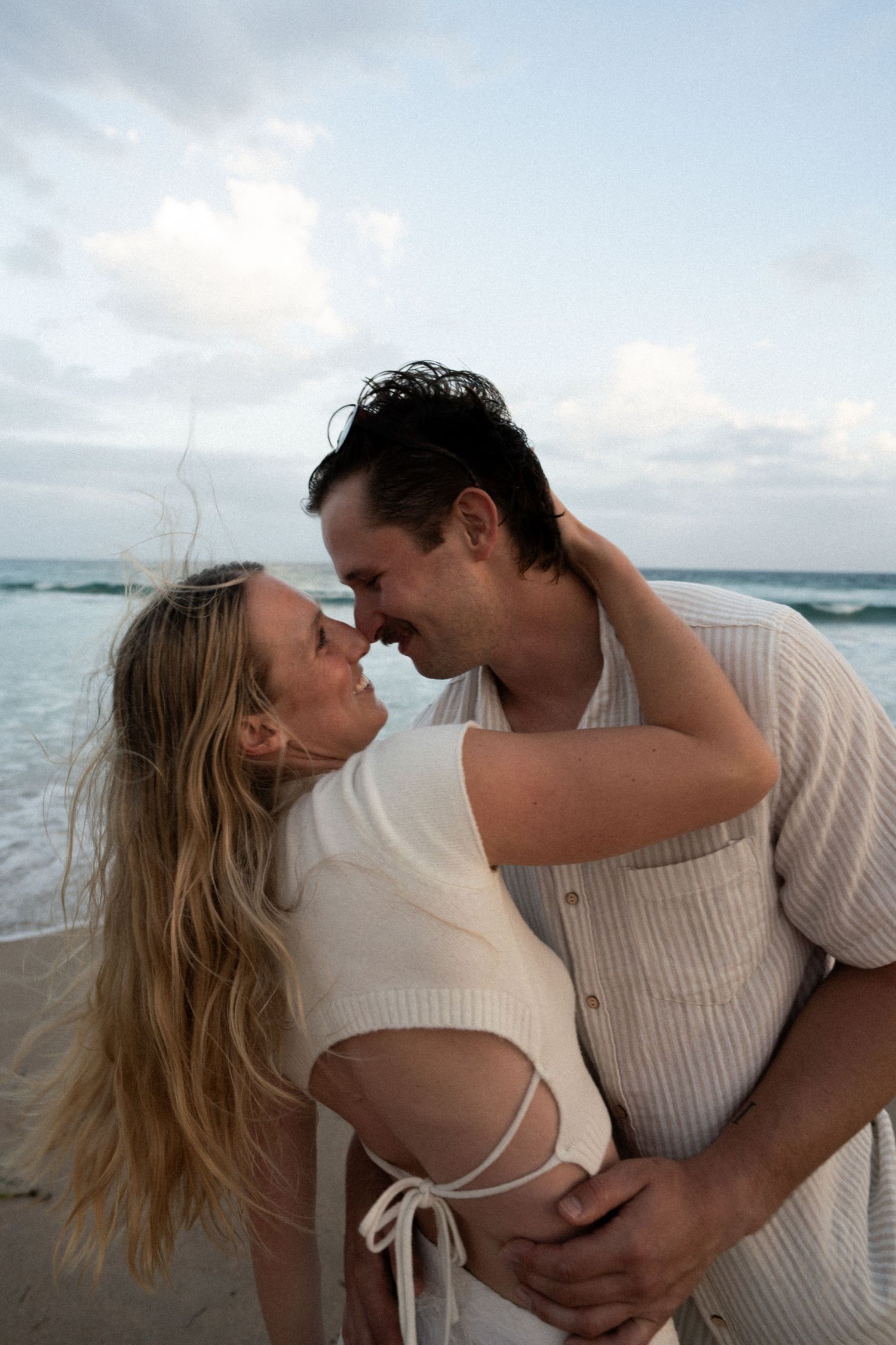 A romantic couple shares intimate moments on a cloudy beach in a series of candid photographs.