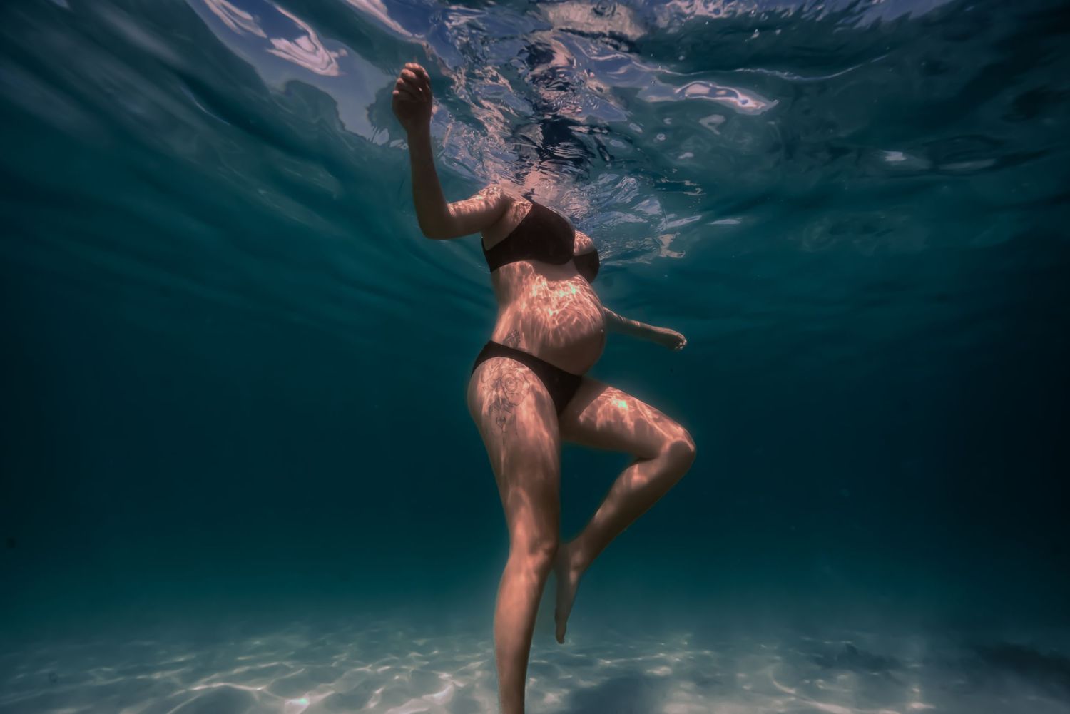 Person swimming underwater in a deep blue ocean, creating graceful movements and bubbles in the sunlit water.