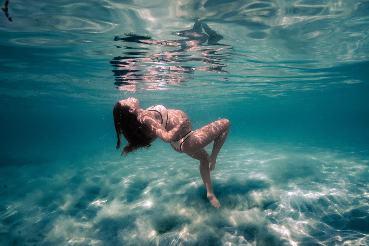 Underwater view of a person floating gracefully in turquoise waters wearing a pink swimsuit.