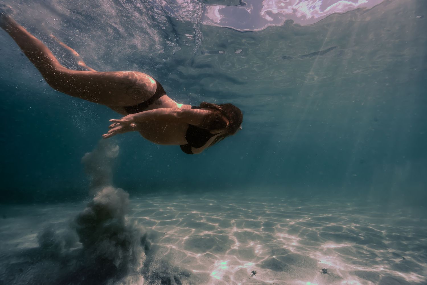 Underwater view of a person swimming in crystal clear blue water with sunlight streaming through the surface.