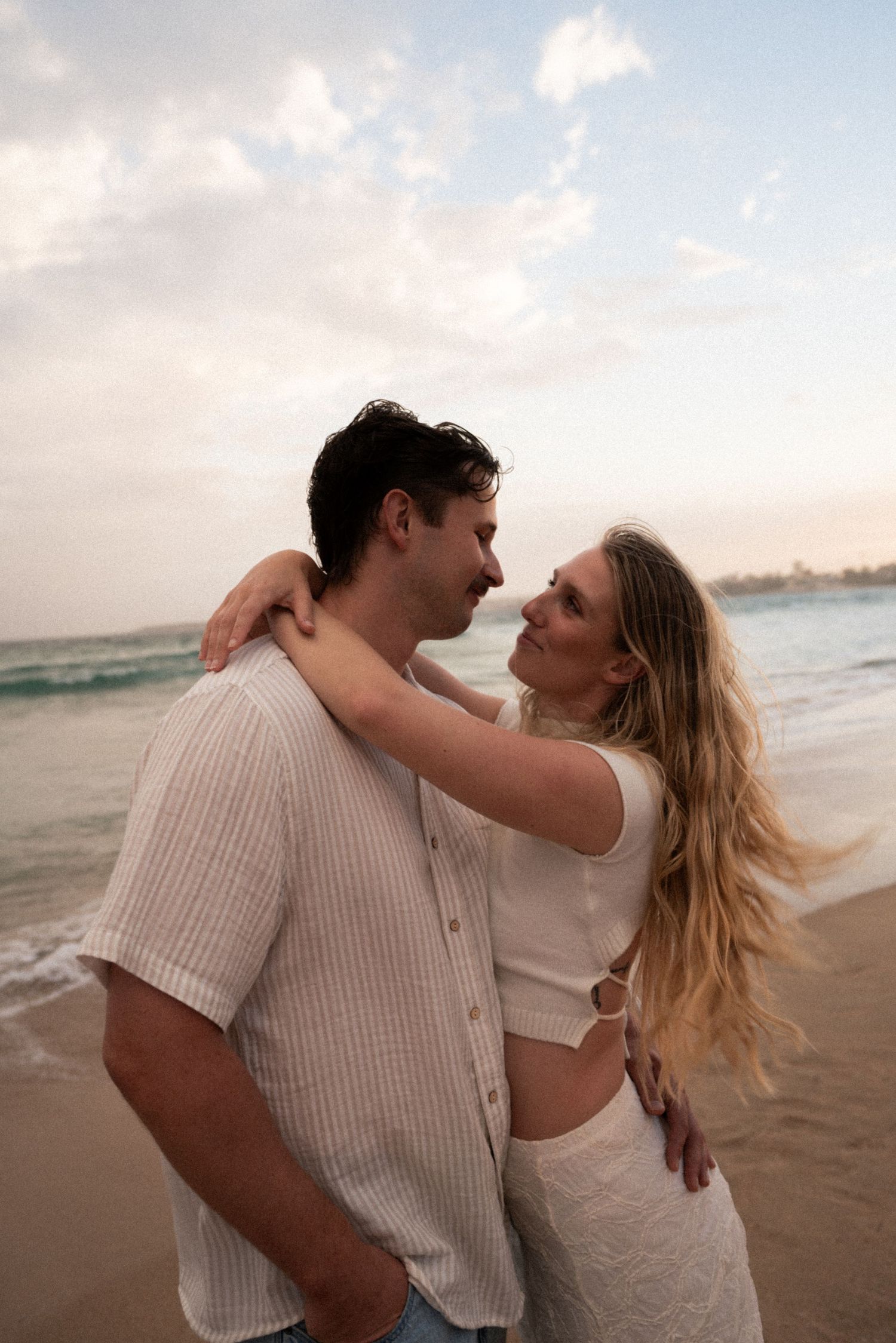 Romantic couple sharing intimate moments on a sandy beach during golden hour.
