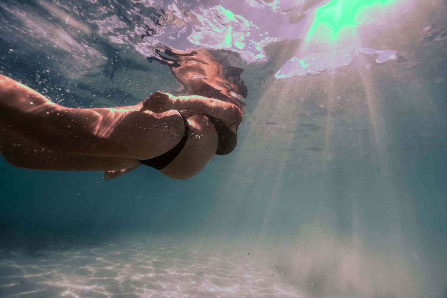Underwater view of swimmers gliding through crystal clear pool water with sunlight streaming from above.
