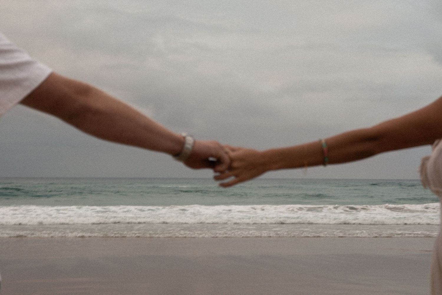 Two hands reach towards each other against a misty ocean background, creating a romantic silhouette at sunset.