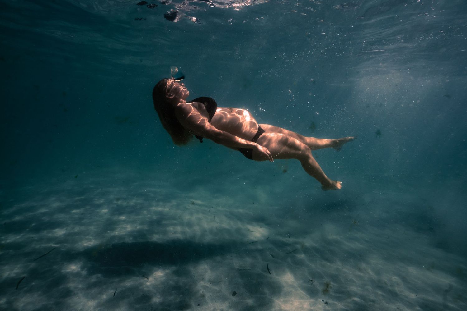 Underwater view of a swimmer floating gracefully in turquoise blue water with sunlight filtering from above.
