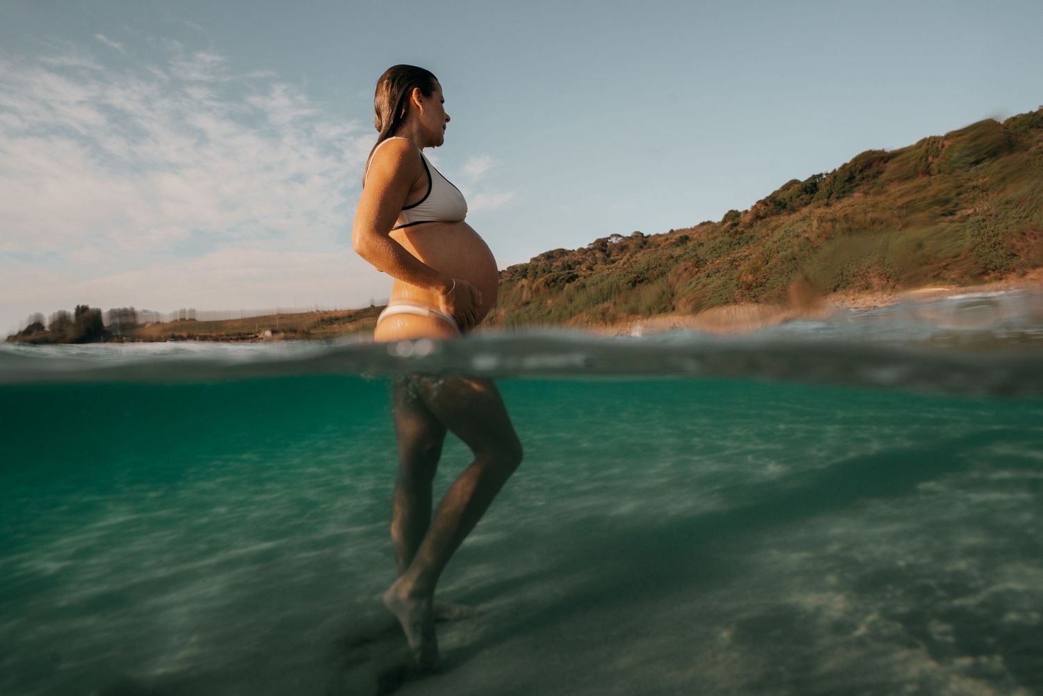 Split-view underwater maternity photo showing a pregnant woman floating in turquoise ocean waters.