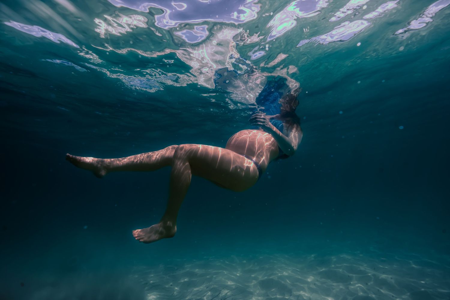 Underwater view of swimmers gliding through crystal clear turquoise water with sunlight filtering from above.