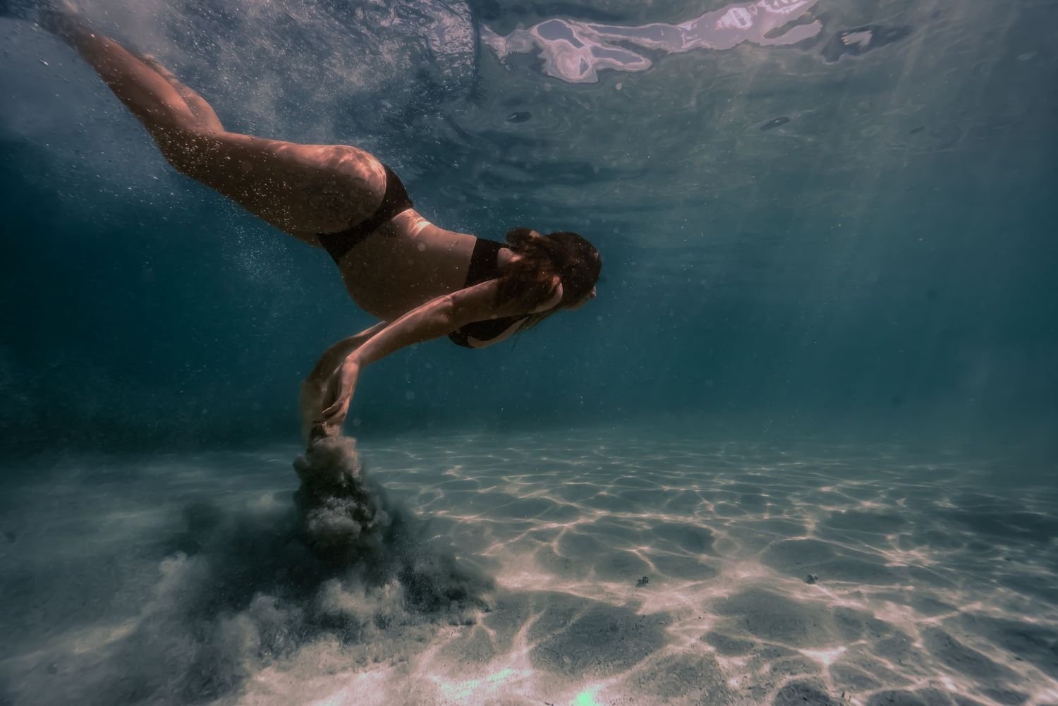 A sequence of underwater photos showing a person swimming and diving in crystal clear blue ocean water.