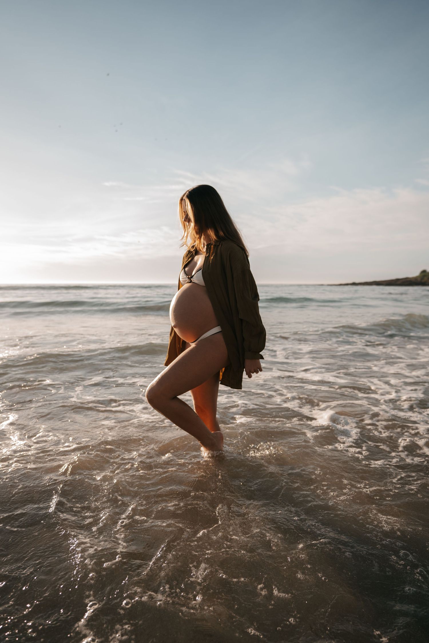 A person sits in shallow ocean waves at sunset creating a serene silhouette against the water and sky.
