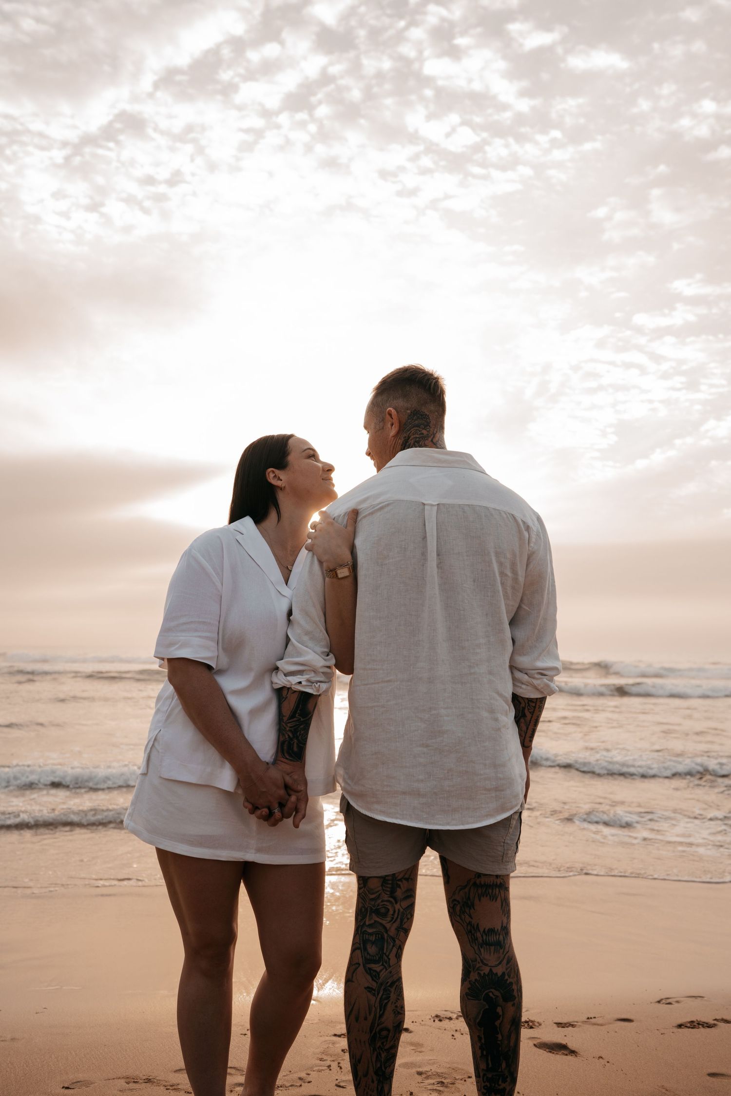 A couple walks along a serene beach at sunset, holding hands and enjoying the ocean view together.
