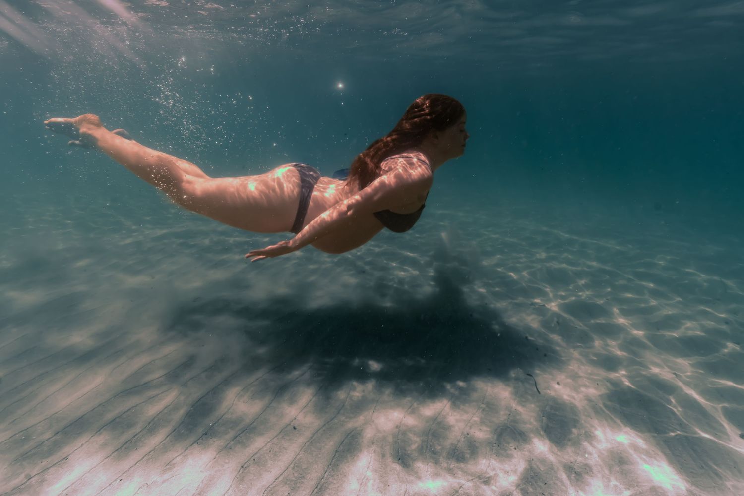 Underwater sequence showing a person gracefully swimming and diving beneath the turquoise ocean surface.