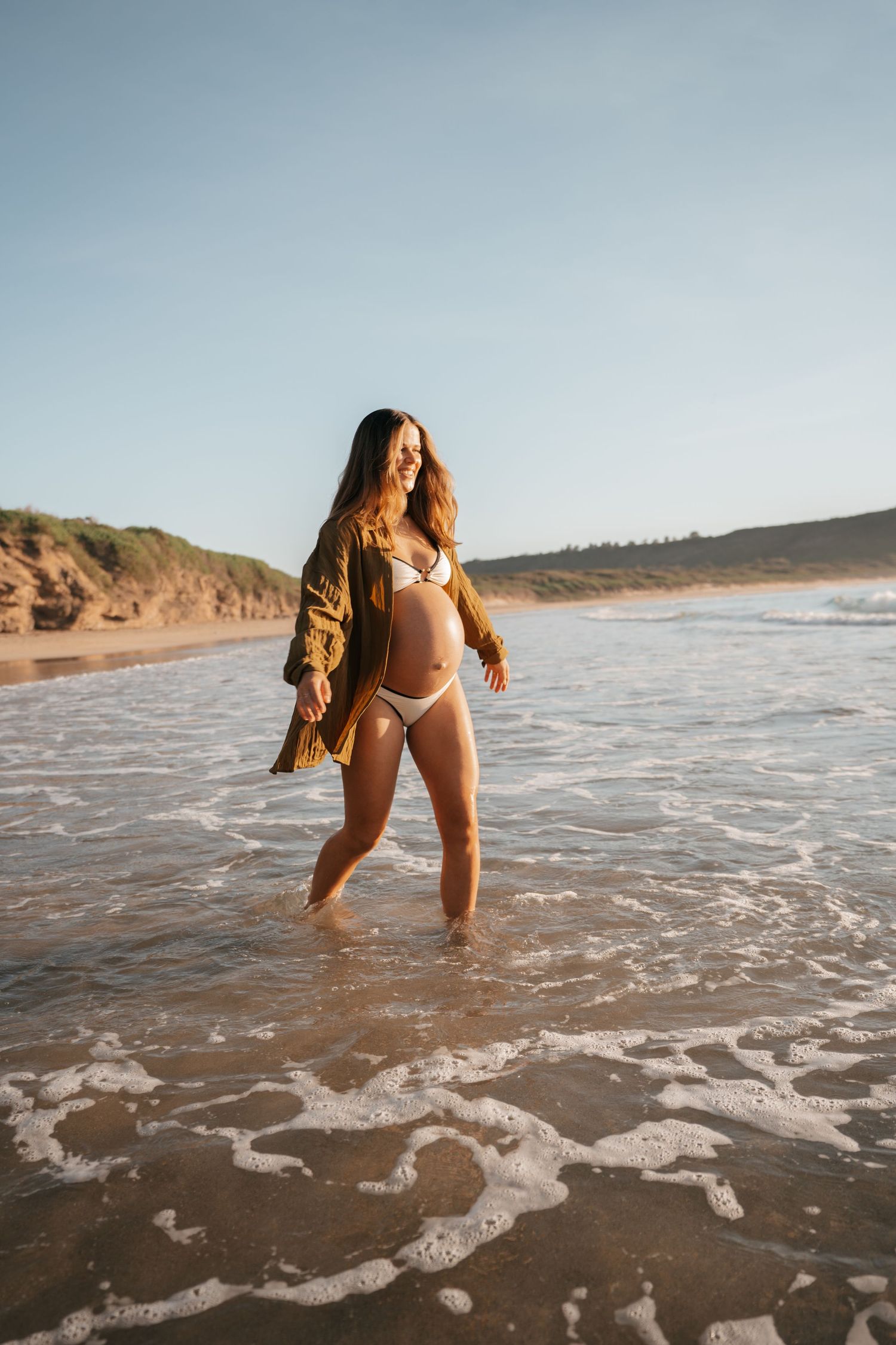 Person enjoying the waves and surf at a scenic beach during golden hour with cliffs in the background.